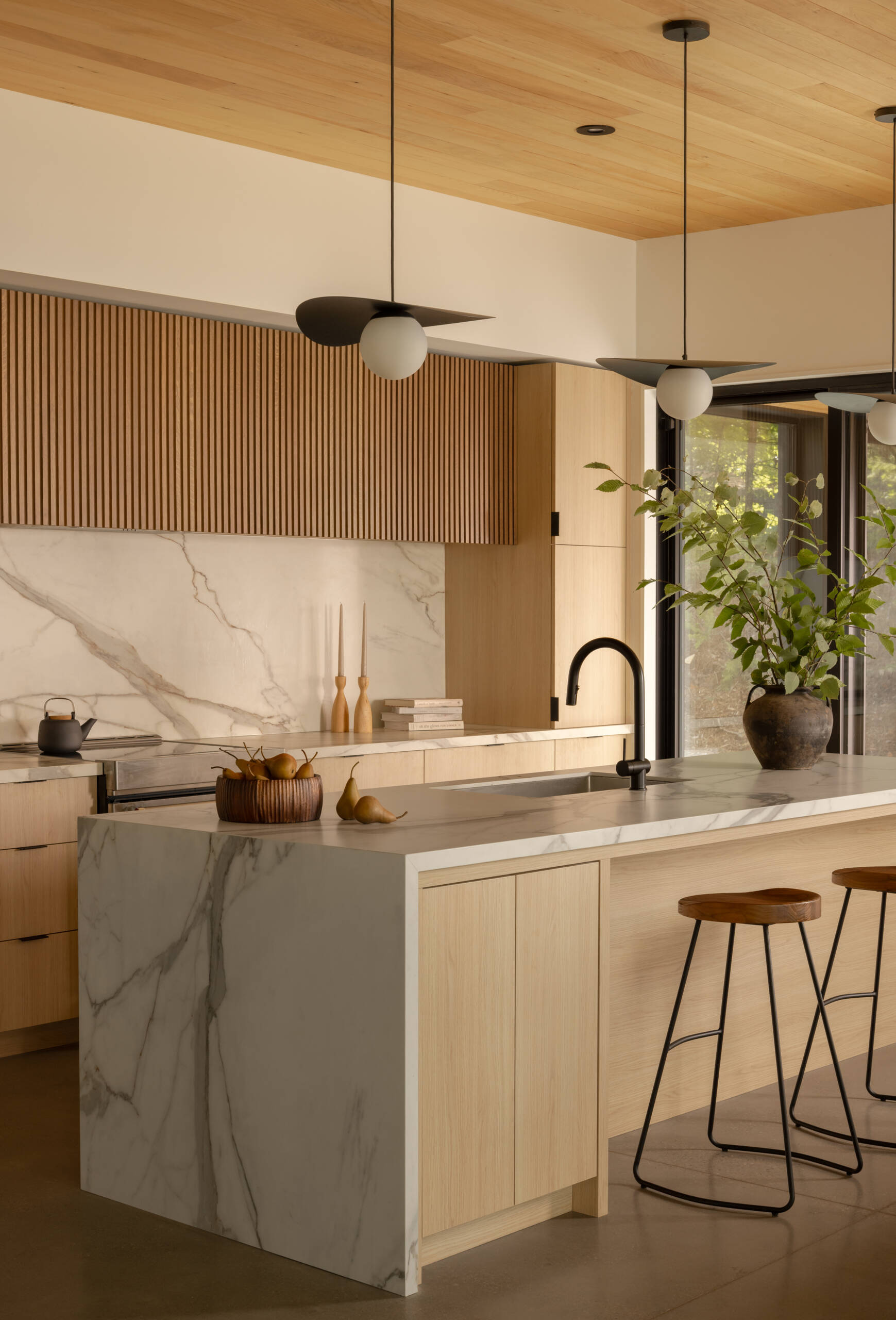 The kitchen, positioned alongside dining and office spaces, follows the same principle: openness to the lake. Here, everyday routines are connected to nature, with natural light softening the contrast between dark exterior and lighter interior tones.