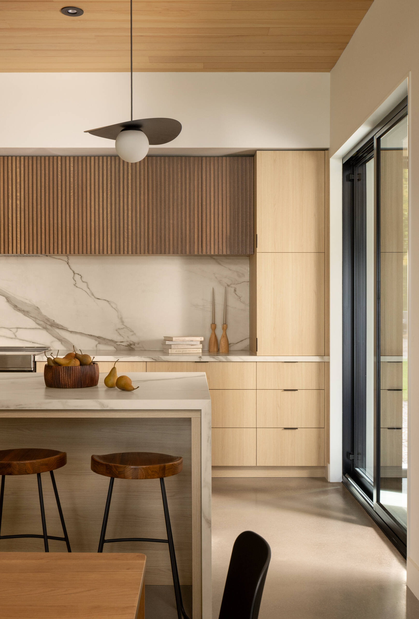 The kitchen, positioned alongside dining and office spaces, follows the same principle: openness to the lake. Here, everyday routines are connected to nature, with natural light softening the contrast between dark exterior and lighter interior tones.