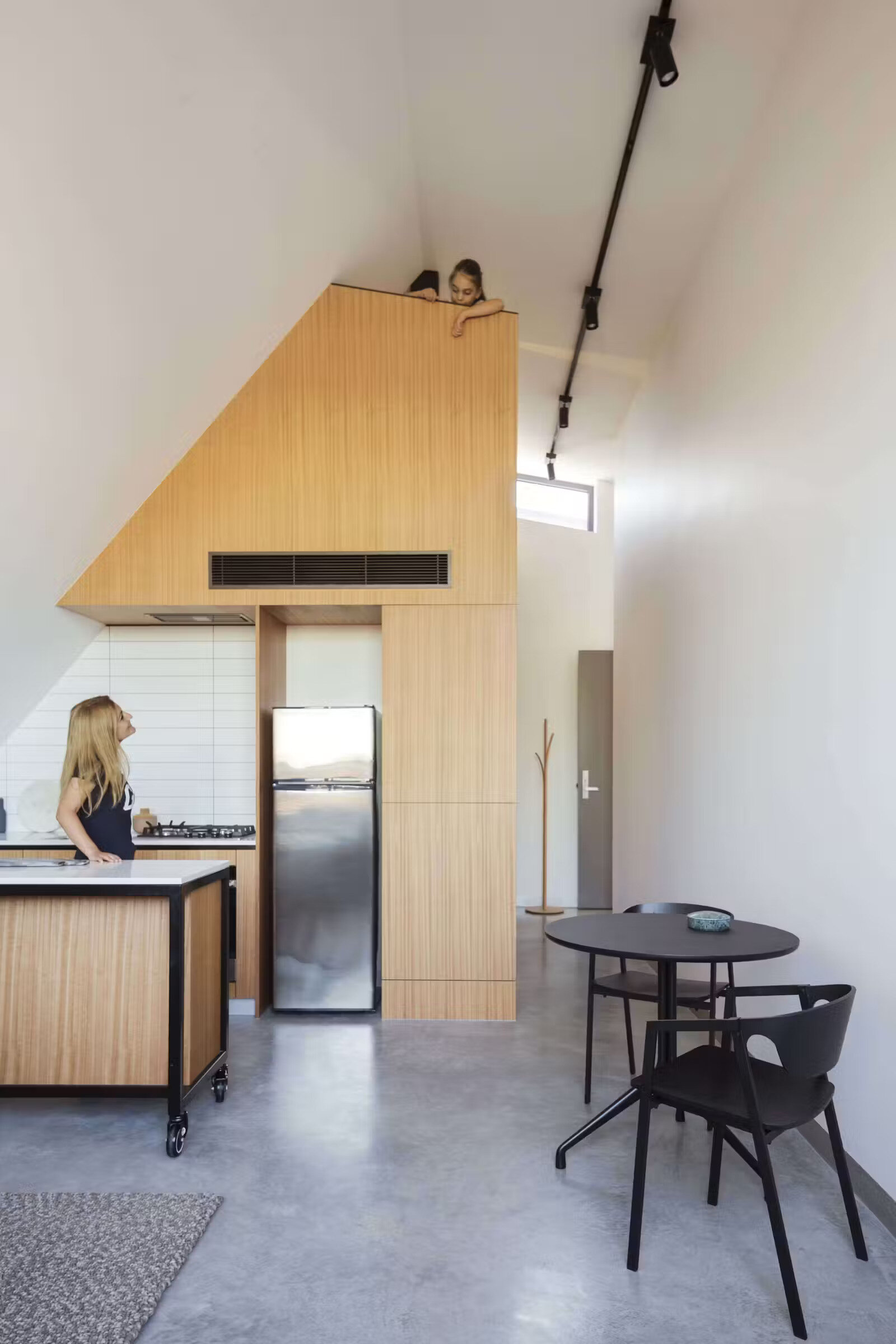 A cozy loft tucked above the kitchen, reached by a ladder and screened with wood slats, adds another dimension to the space.