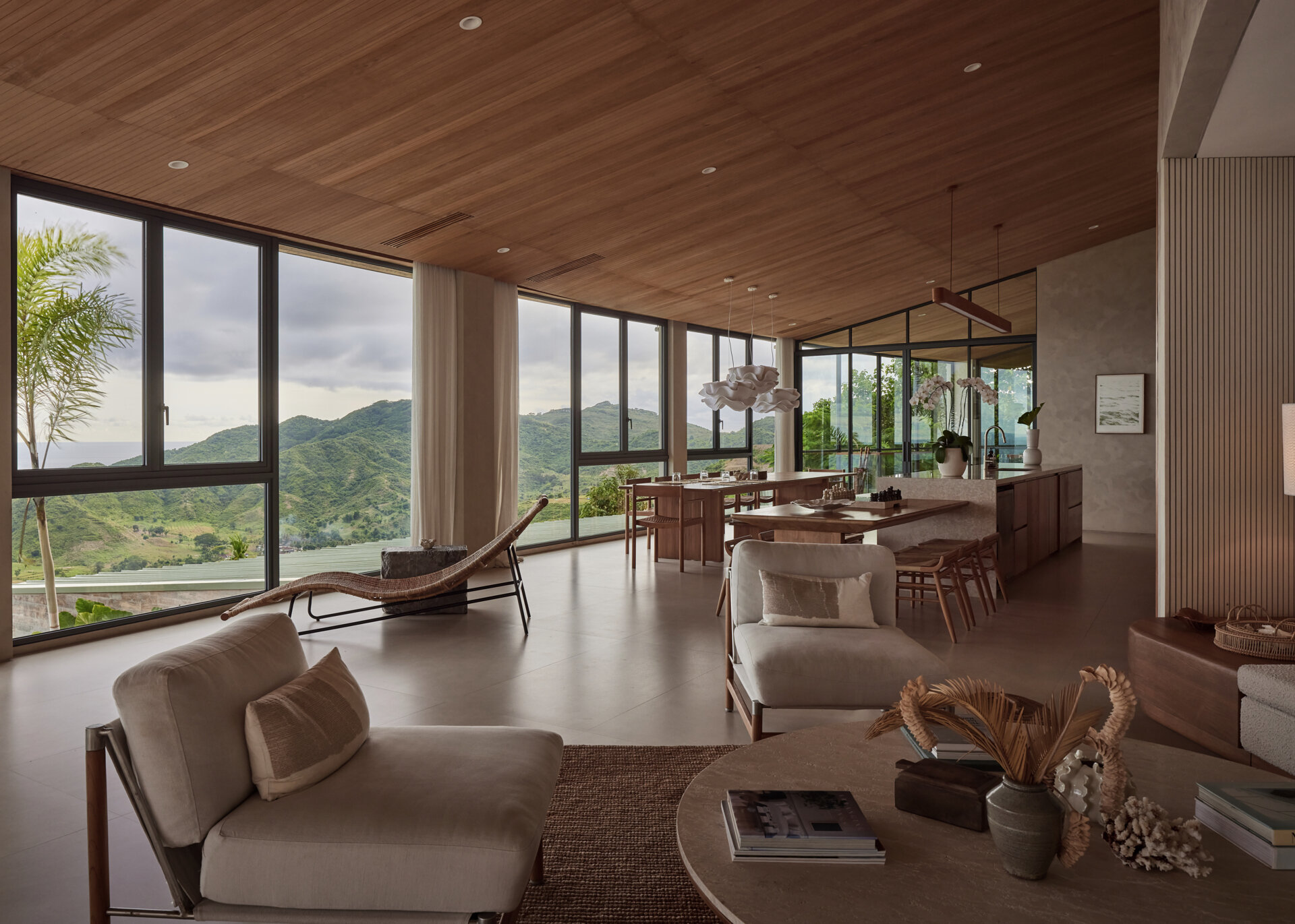 The social areas open up after the entry, bringing together the living room, dining room, and kitchen. Walls of windows fills the interior with an abundance of natural light, while the wood ceiling and furniture adds warmth to the home.