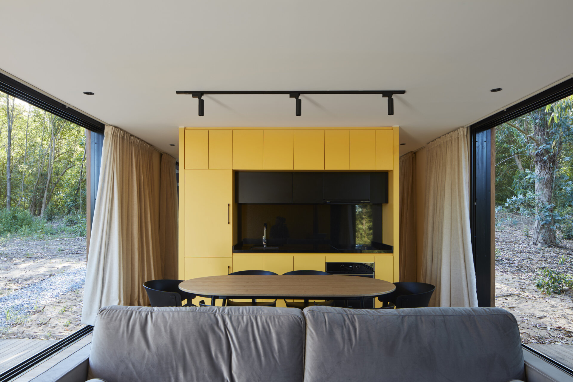 A small forest home with an open living room, dining area, and kitchen. The yellow accent wall and kitchen add a pop of color.