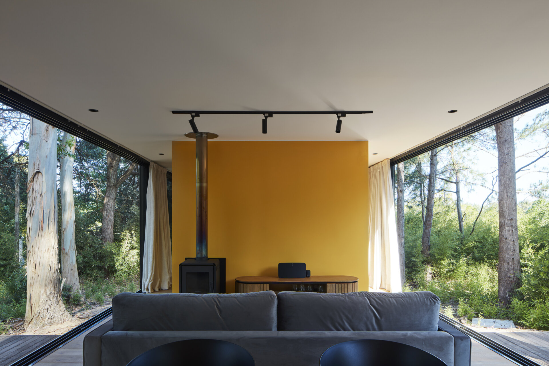 A small forest home with an open living room, dining area, and kitchen. The yellow accent wall and kitchen add a pop of color.