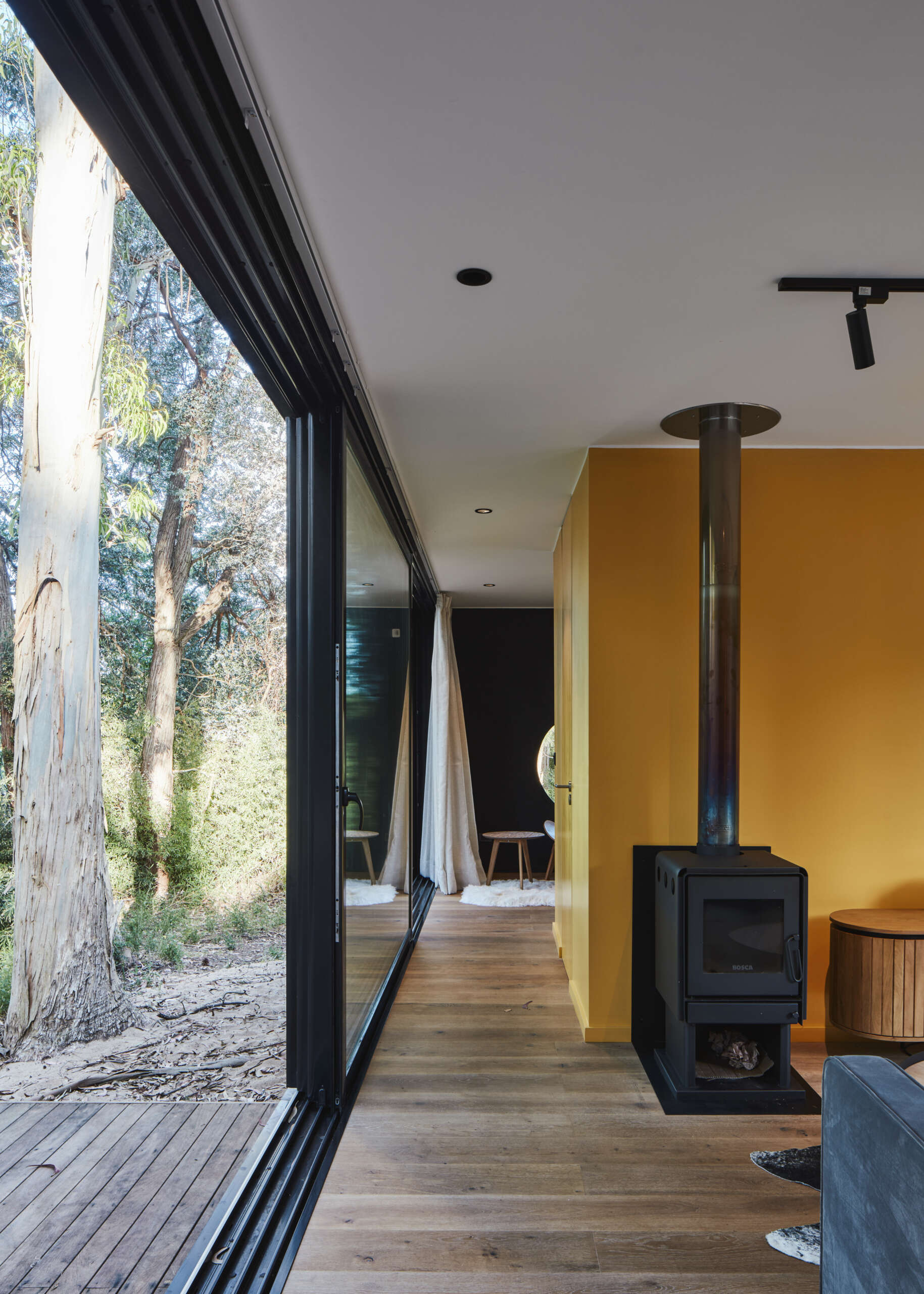 A small forest home with an open living room, dining area, and kitchen. The yellow accent wall and kitchen add a pop of color.