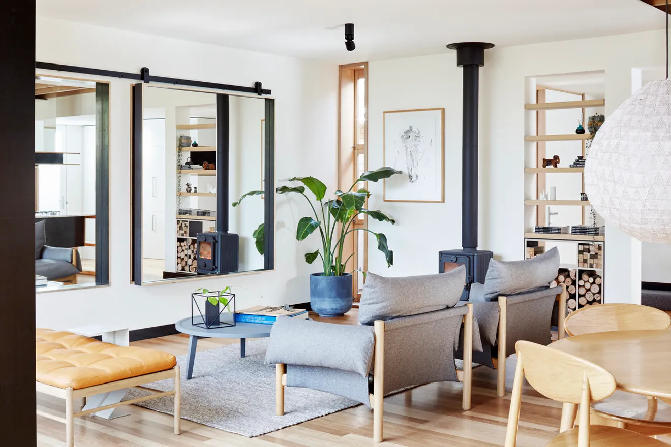 The living area is cozy and practical. Open shelving doubles as storage for stacked firewood, ready to feed the wood-burning fireplace. A large wall mirror creates a greater sense of space while cleverly hiding the television when it’s not in use.