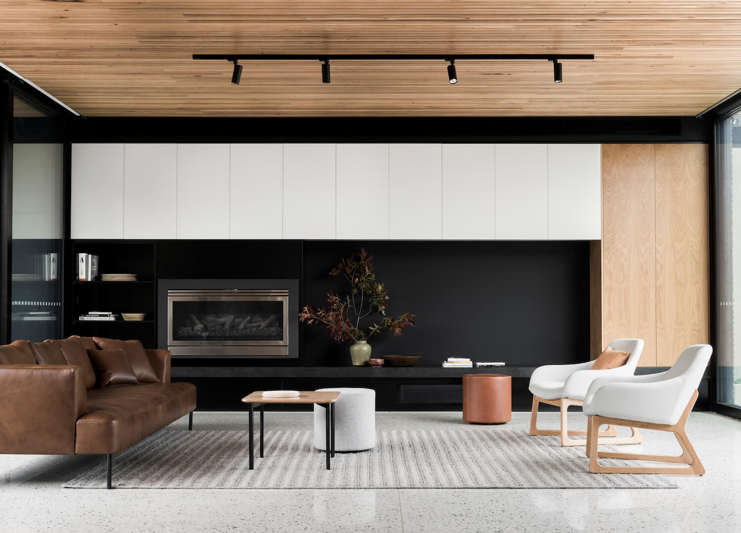 The interiors are designed with contrast in mind. A timber batten ceiling draws the eye through the space, guiding movement while warming the atmosphere. Below, white concrete flooring keeps the rooms light and airy. In the living area, a black feature wall defines the space within the open-plan layout, balancing the softer tones of wood and brick.
