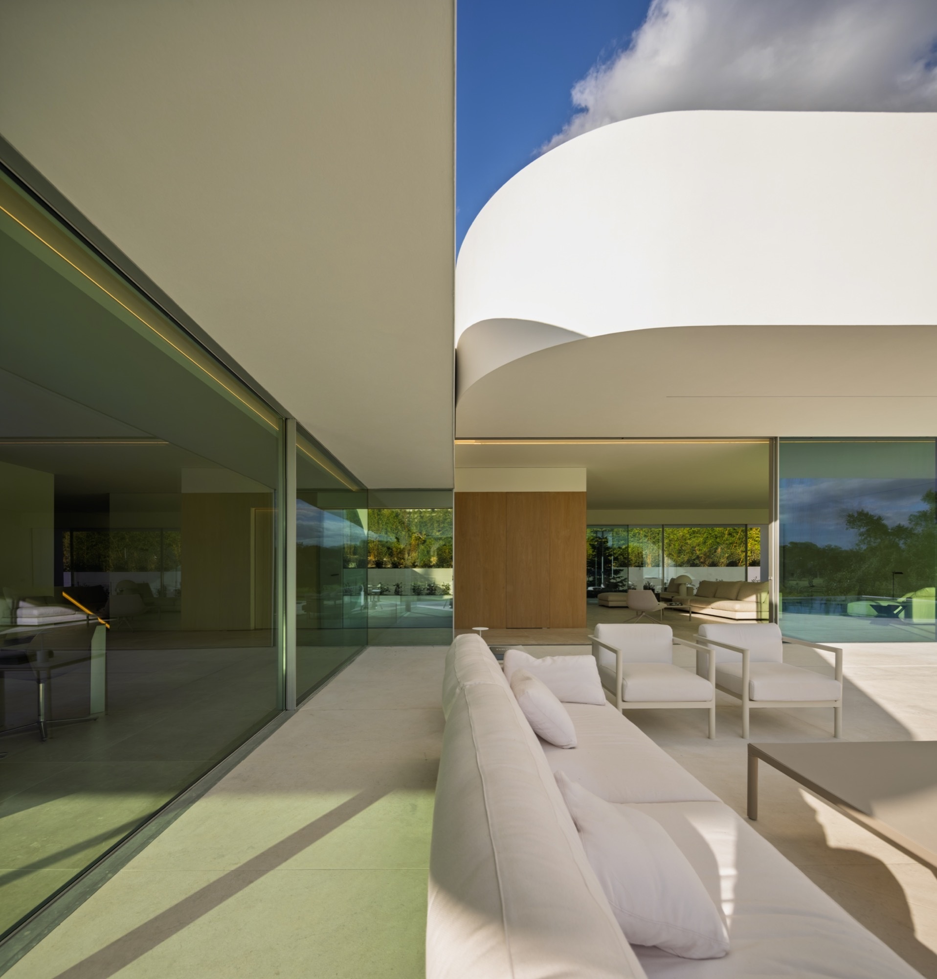 The sheltered terrace, formed by the shifted volumes, is oriented toward the southeast landscape. Curved edges define its open-air spaces, blending fluidly with the straight lines of the home’s geometry. This creates both a comfortable outdoor environment and continuity between interior and exterior.