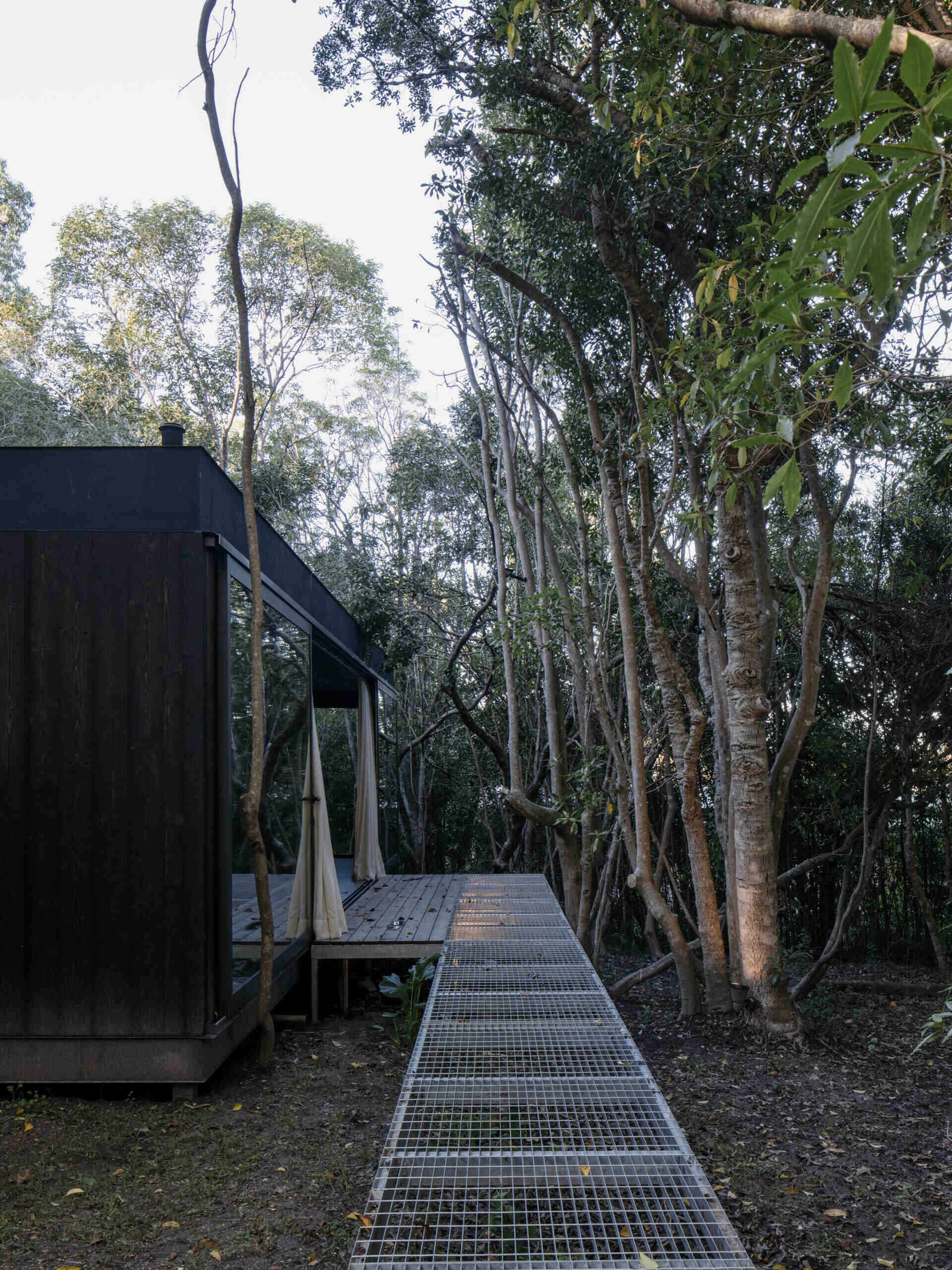 A discreet metal bridge extends from the entrance of this prefab home, emphasizing the idea of a structure that floats over the terrain rather than imposing on it. This gesture reinforces the balance between architecture and landscape.