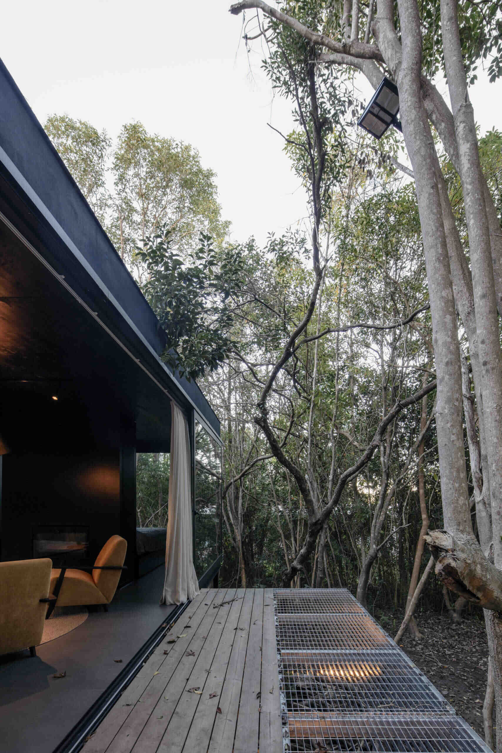A discreet metal bridge extends from the entrance of this prefab home, emphasizing the idea of a structure that floats over the terrain rather than imposing on it. This gesture reinforces the balance between architecture and landscape.