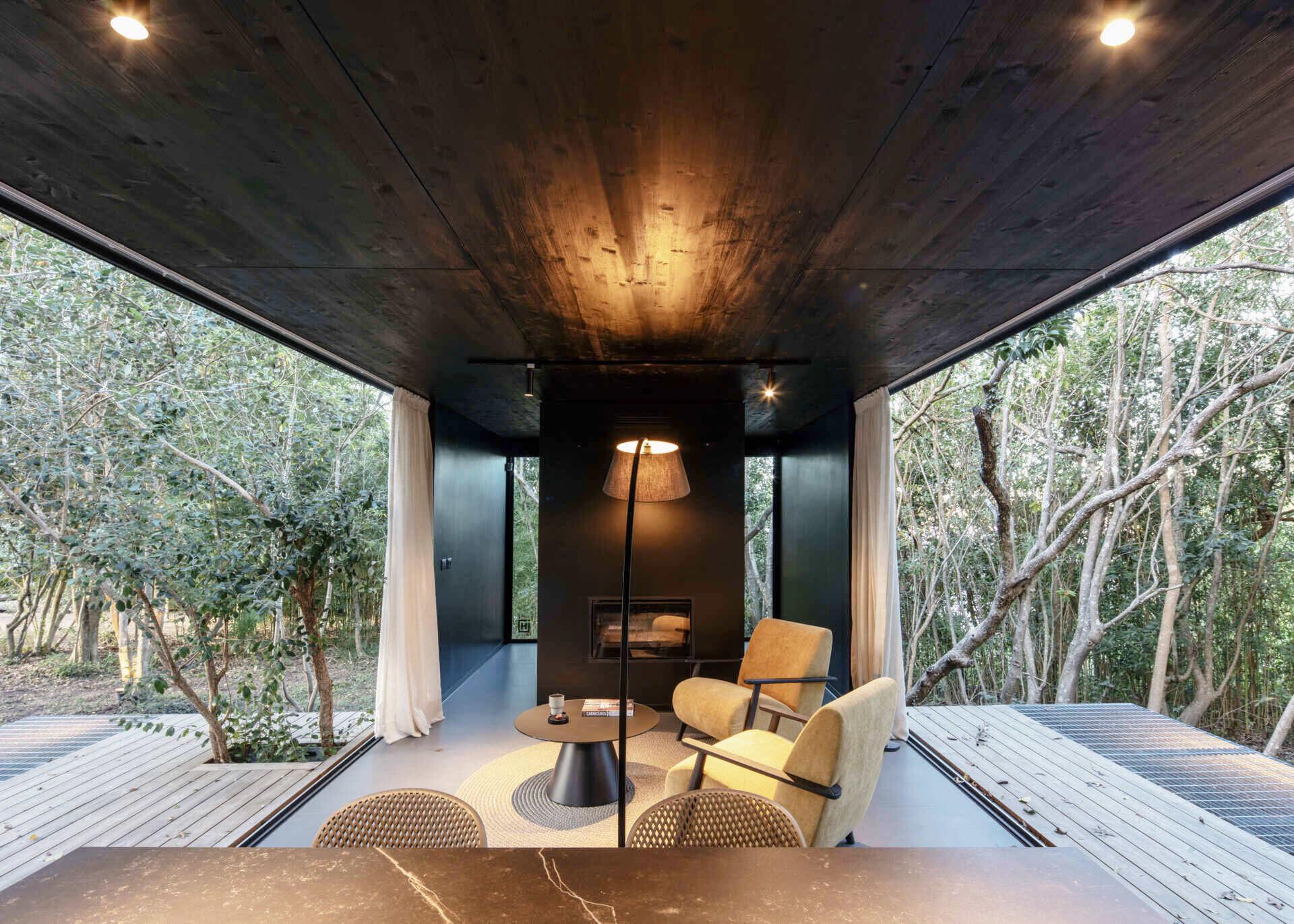 A small prefab home has sliding panels that blur the boundaries between indoors and outdoors, allowing the social space to open fully on both sides.
