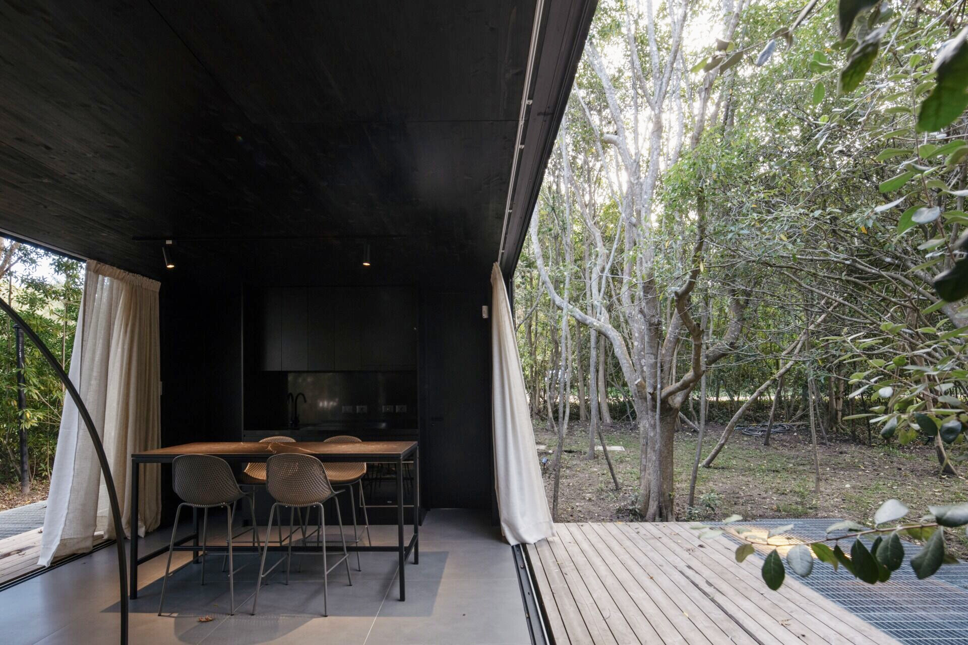 A small prefab home has sliding panels that blur the boundaries between indoors and outdoors, allowing the social space to open fully on both sides.