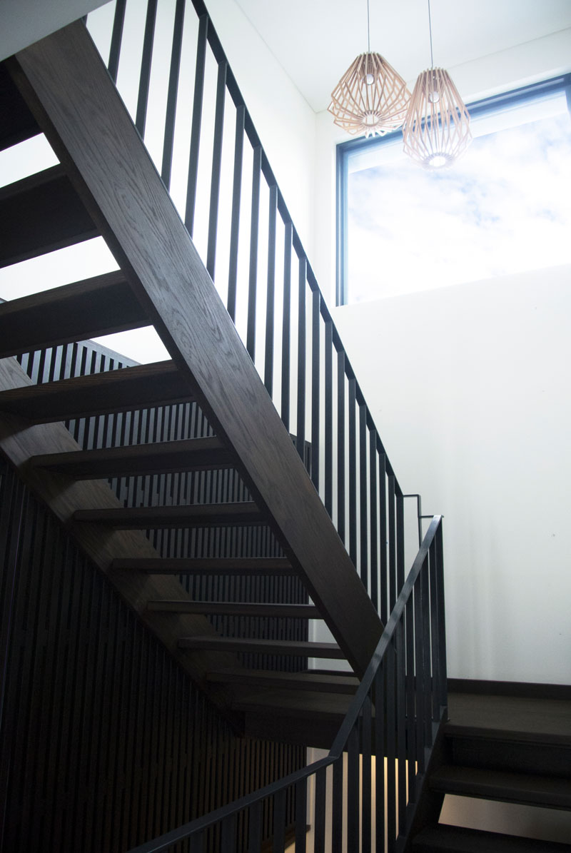The dark wood staircase is both functional and sculptural, guiding movement through the house while framing bush views along the way. A large window alongside the stairs ensures every step is naturally lit.