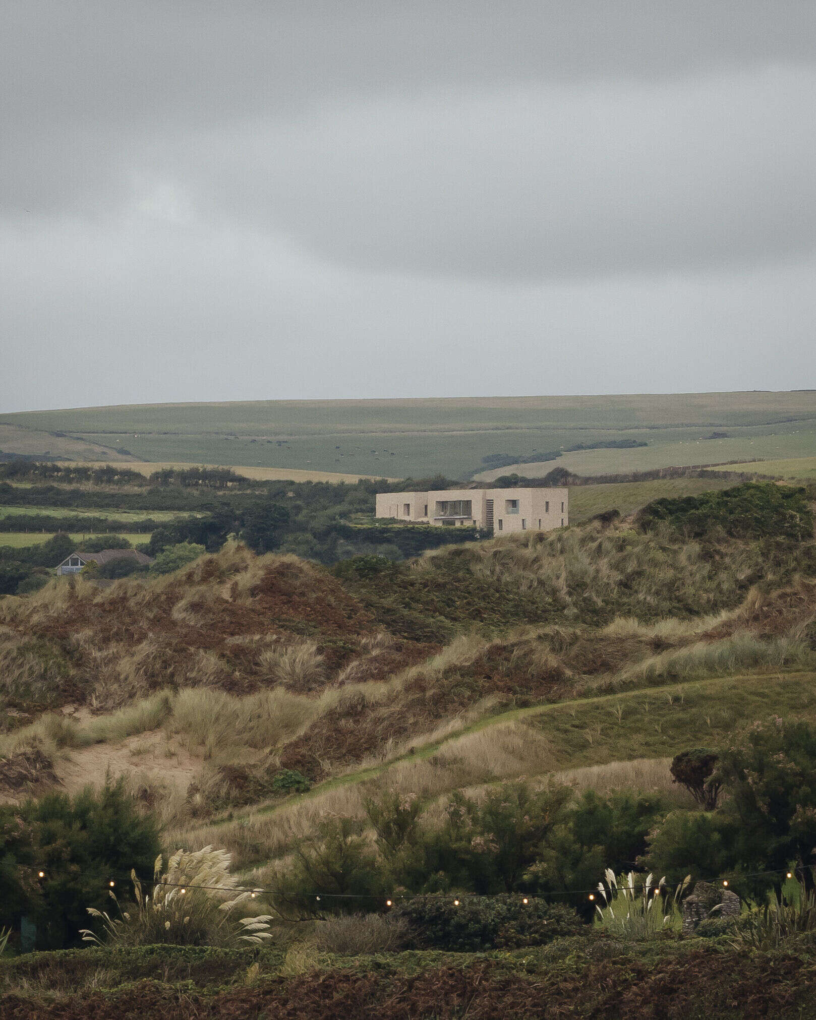 This modern home is built from pale Purbeck stone, with a curved facade that follows the natural bend of the site. A green roof hides solar panels, while coastal grasses and granite landscaping root the home into the hillside.