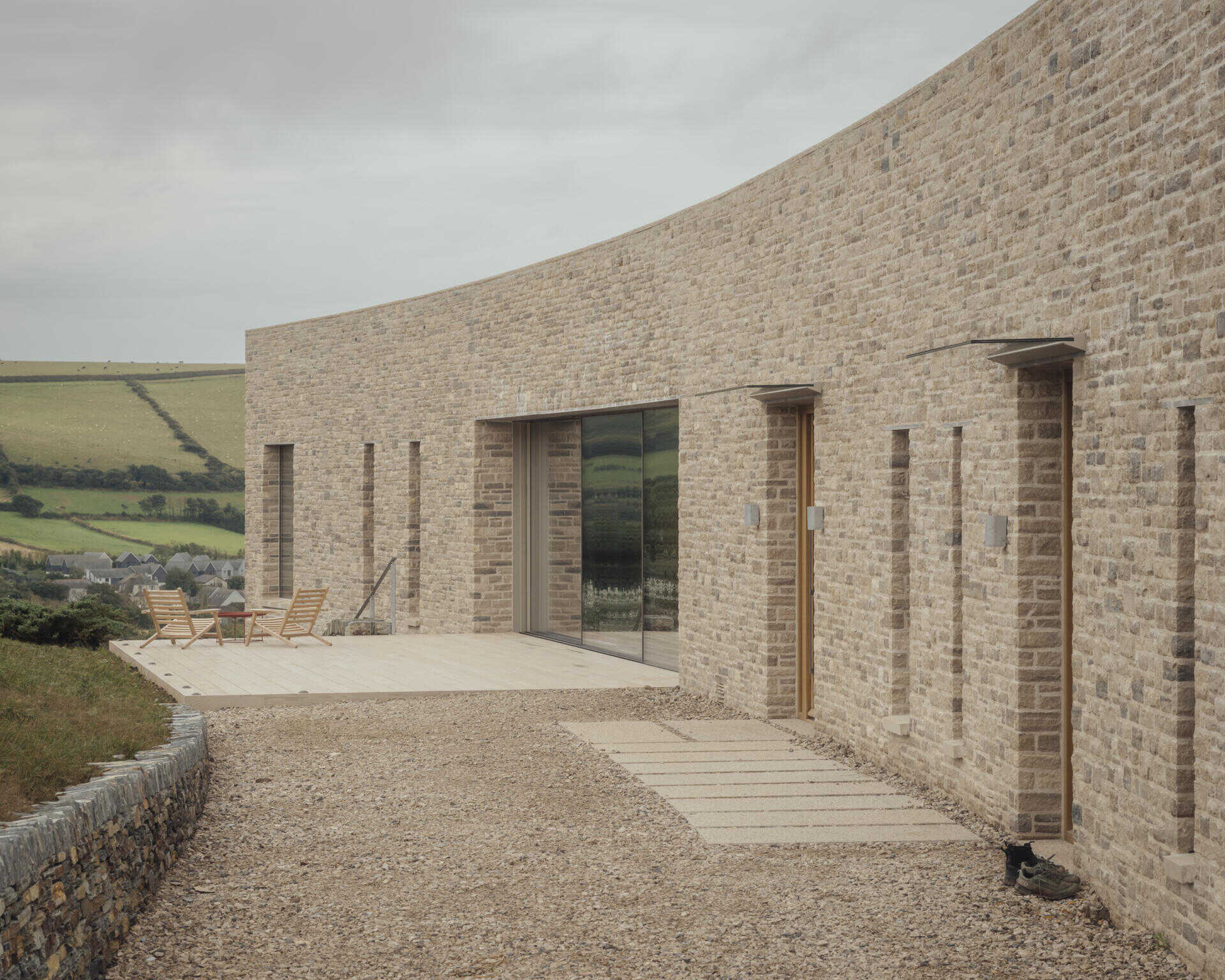 This modern home is built from pale Purbeck stone, with a curved facade that follows the natural bend of the site. A green roof hides solar panels, while coastal grasses and granite landscaping root the home into the hillside.
