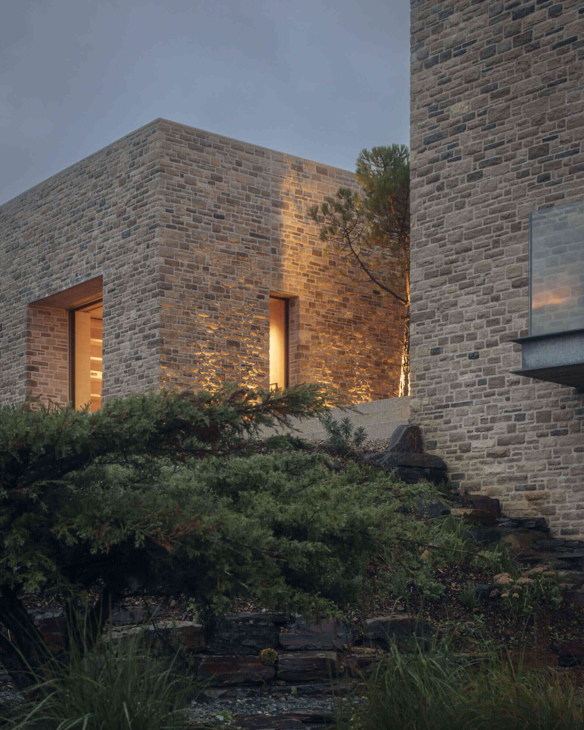 This modern home is built from pale Purbeck stone, with a curved facade that follows the natural bend of the site. A green roof hides solar panels, while coastal grasses and granite landscaping root the home into the hillside.