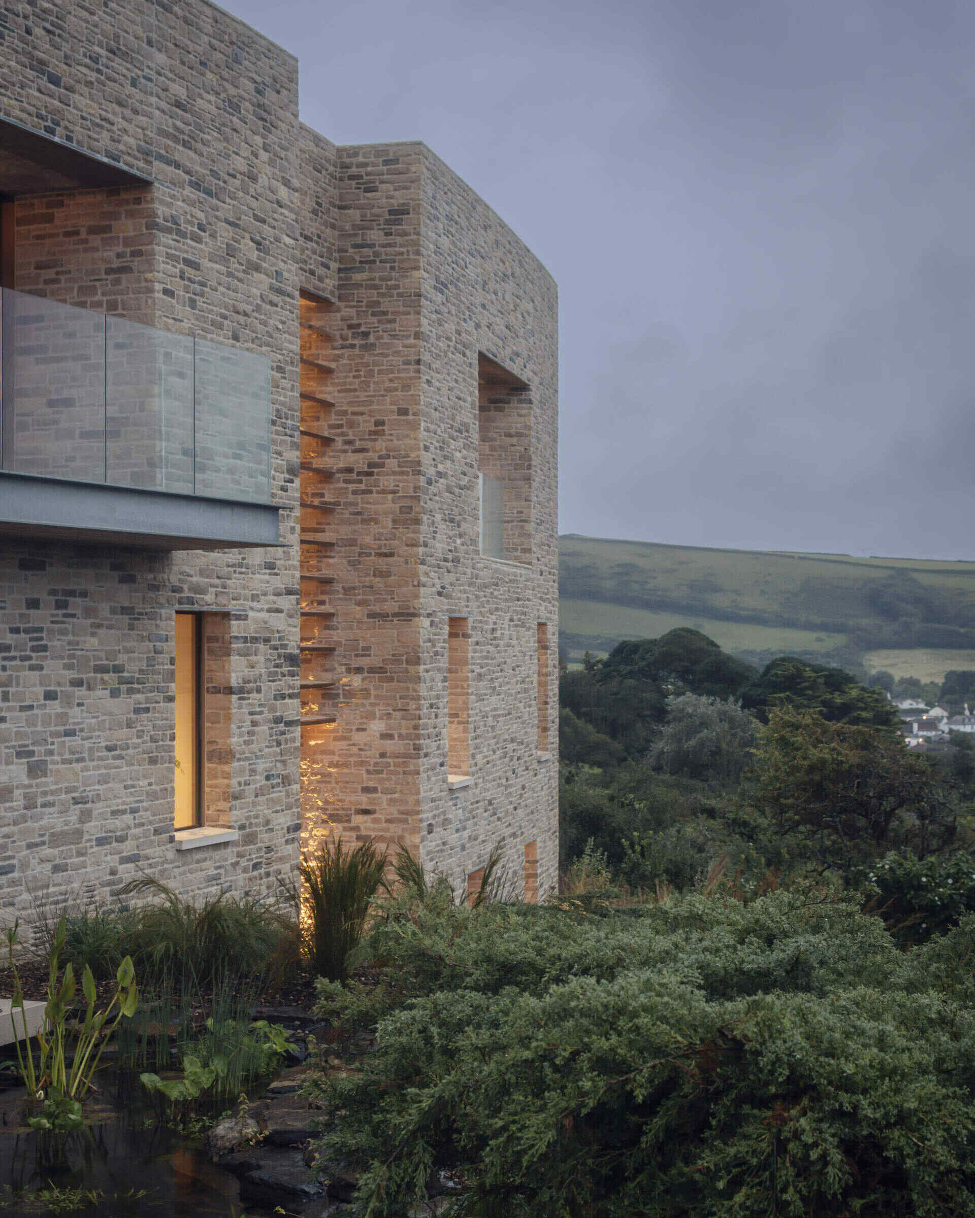 This modern home is built from pale Purbeck stone, with a curved facade that follows the natural bend of the site. A green roof hides solar panels, while coastal grasses and granite landscaping root the home into the hillside.