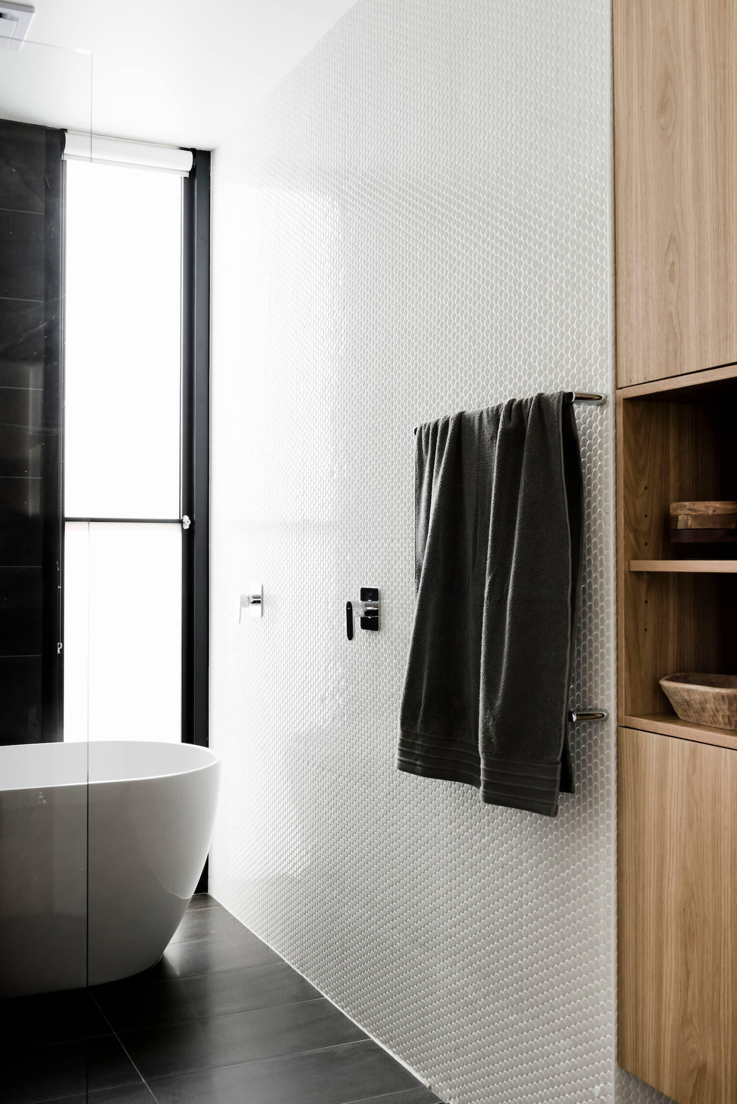 The bathroom takes on a bolder, contemporary tone. Large dark tiles are paired with smaller white ones, creating visual balance. Touches of wood soften the space, ensuring it remains warm rather than stark. The result is a bathroom that feels both sophisticated and inviting.