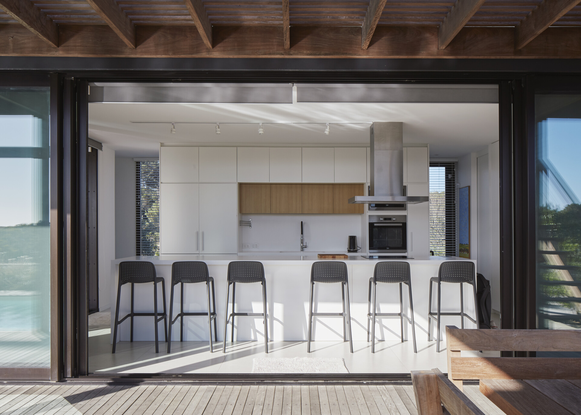 A large kitchen with a central island, white cabinets, and a wood accent, serves as the heart of the second module. The island doubles as a dining space, balancing casual meals with generous room for gatherings.