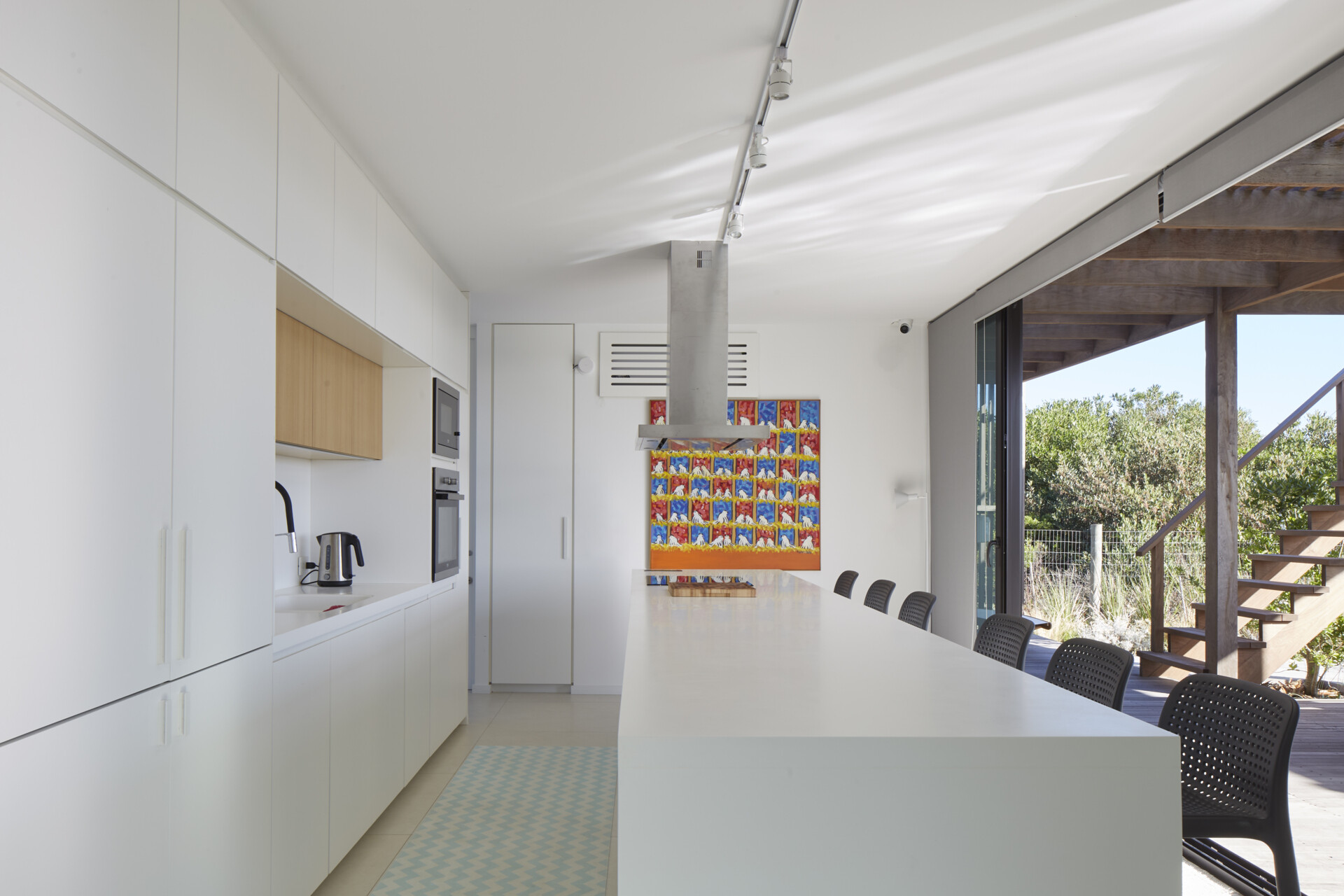 A large kitchen with a central island, white cabinets, and a wood accent, serves as the heart of the second module. The island doubles as a dining space, balancing casual meals with generous room for gatherings.