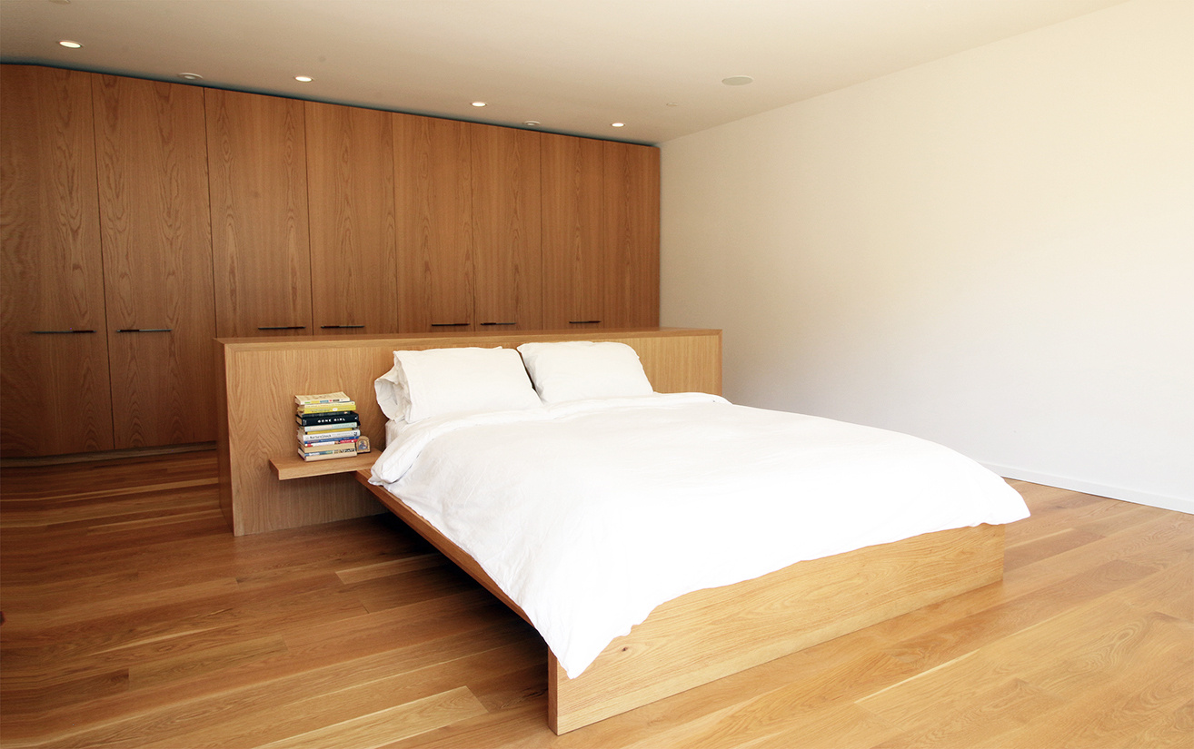 A serene master bedroom with oak finishes and sliding doors to a desert patio inside a modern mountain home.
