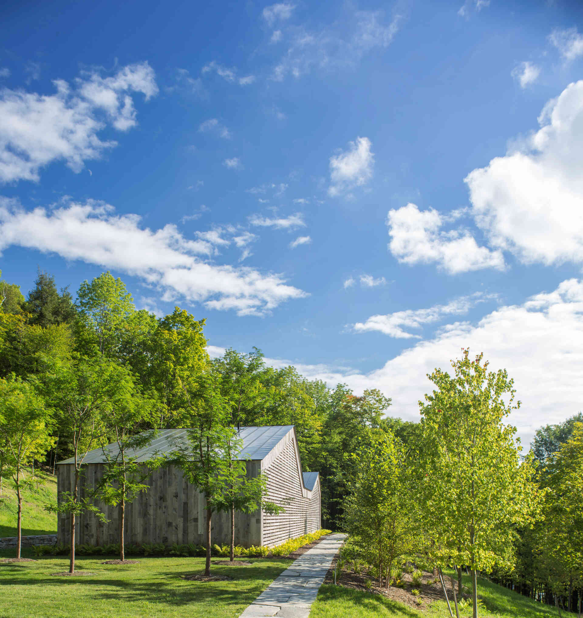 A Vermont guest house takes its shape from the classic woodshed, with gabled roofs that reimagine a familiar rural form. The house is clad in reclaimed snow fencing, weathered boards that give the structure instant character and texture.