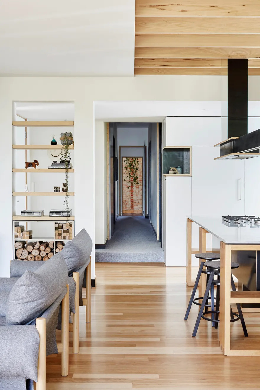 Inside the extension, one open space houses the kitchen, dining, and living areas. White walls keep the atmosphere bright, while natural wood adds warmth and texture. Folding glass doors open directly to the backyard, making the connection between indoors and outdoors seamless.