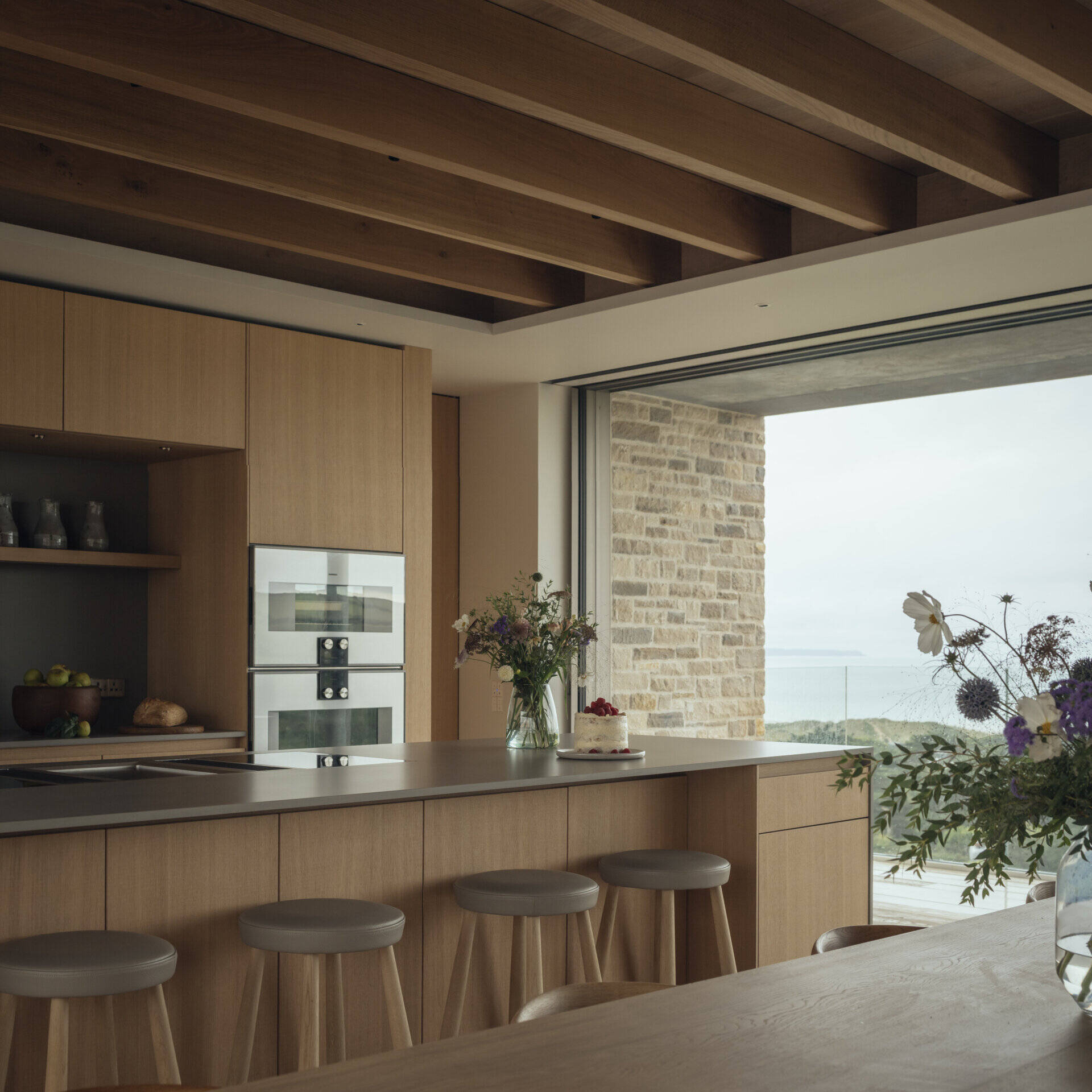 The kitchen blends function with crafted detail. McLean Quinlan’s custom joinery appears here in smooth and rough-sawn oak, paired with brushed brass hardware. The flooring is engineered oak, offset by plaster walls and large ceramic tiles that provide both texture and warmth. The design ensures practicality while retaining a sense of tactile luxury.