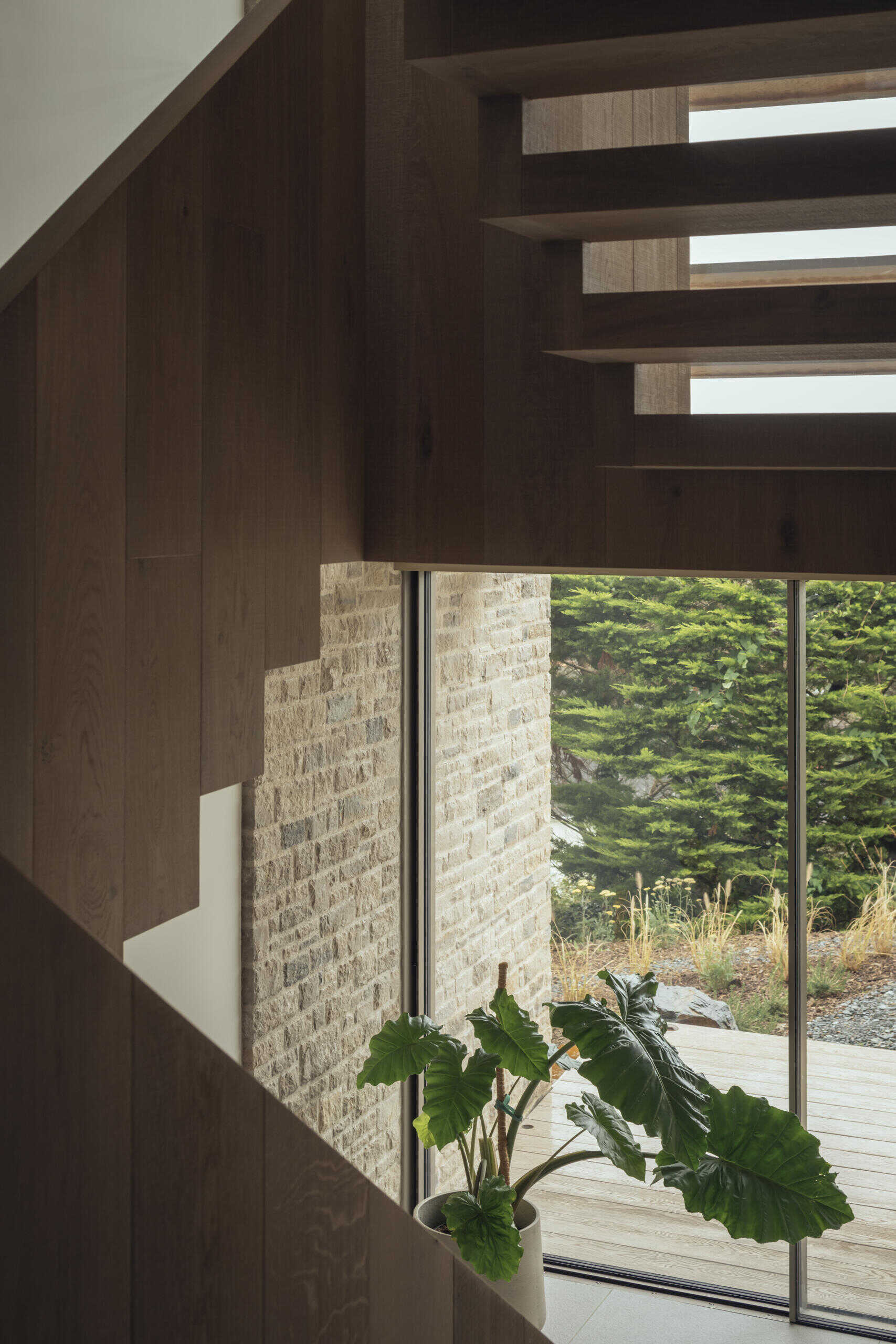 At the south side of the house, a stair hall becomes an architectural feature in itself. Glazed walls bring in daylight, while angled oak slats filter sun and add rhythm to the stone facade. Oak treads connect the levels, carrying light between floors.