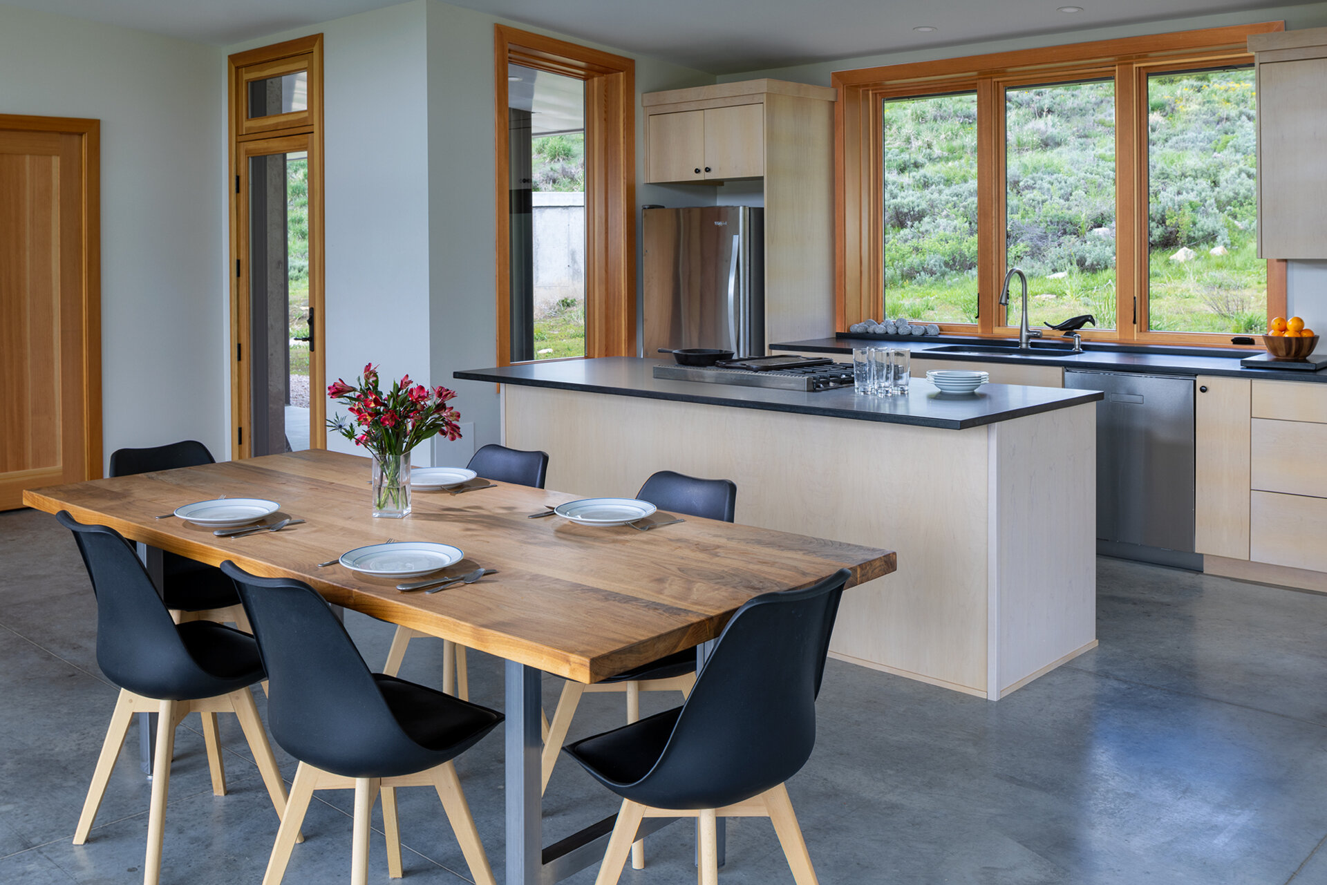 The living room, dining area, and kitchen all share the great room. In the kitchen, honed black granite countertops provide both durability and refinement. A restrained material palette throughout the dining and cooking areas underscores the cabin’s emphasis on craft and practicality while keeping the focus on its natural surroundings.