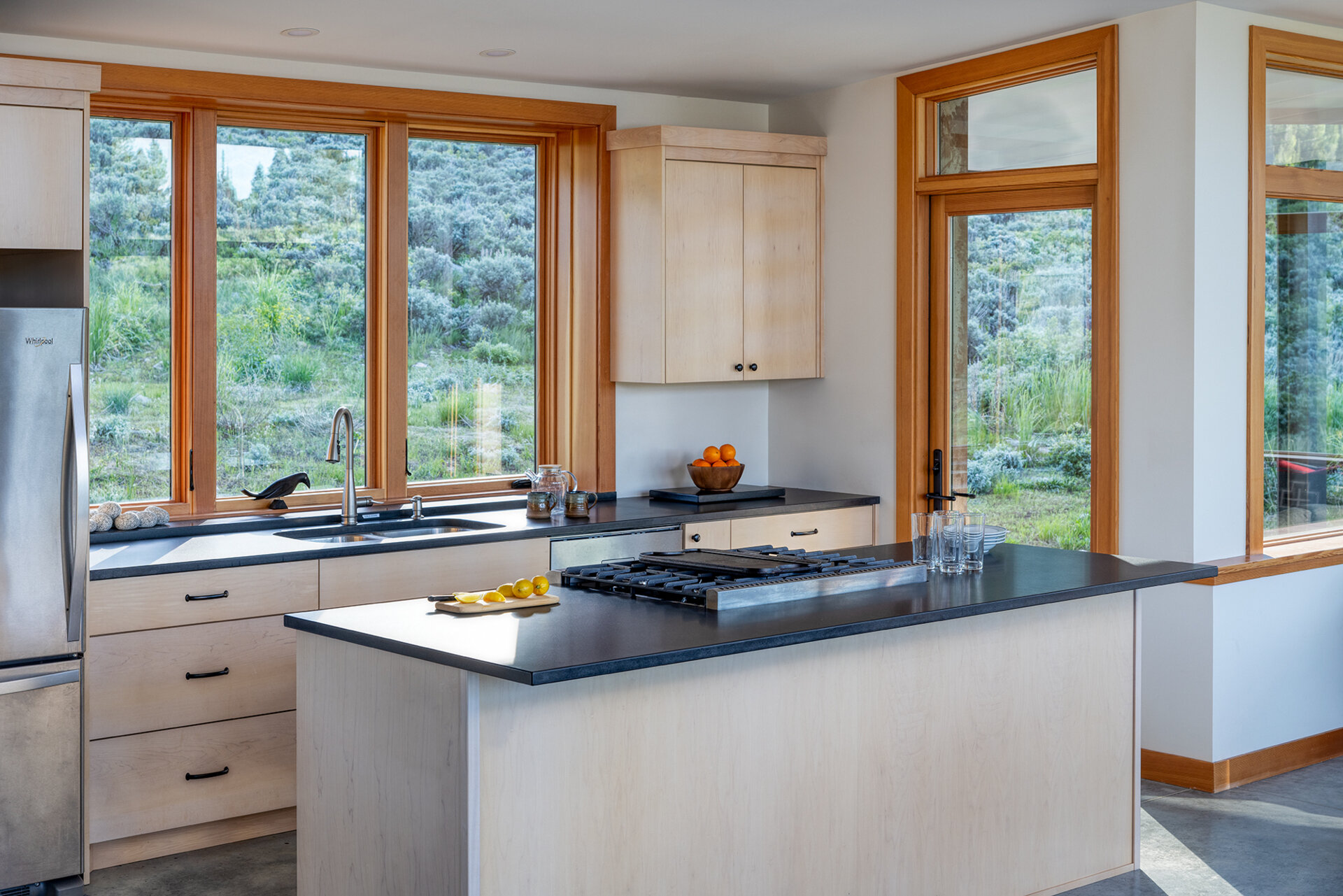 The living room, dining area, and kitchen all share the great room. In the kitchen, honed black granite countertops provide both durability and refinement. A restrained material palette throughout the dining and cooking areas underscores the cabin’s emphasis on craft and practicality while keeping the focus on its natural surroundings.