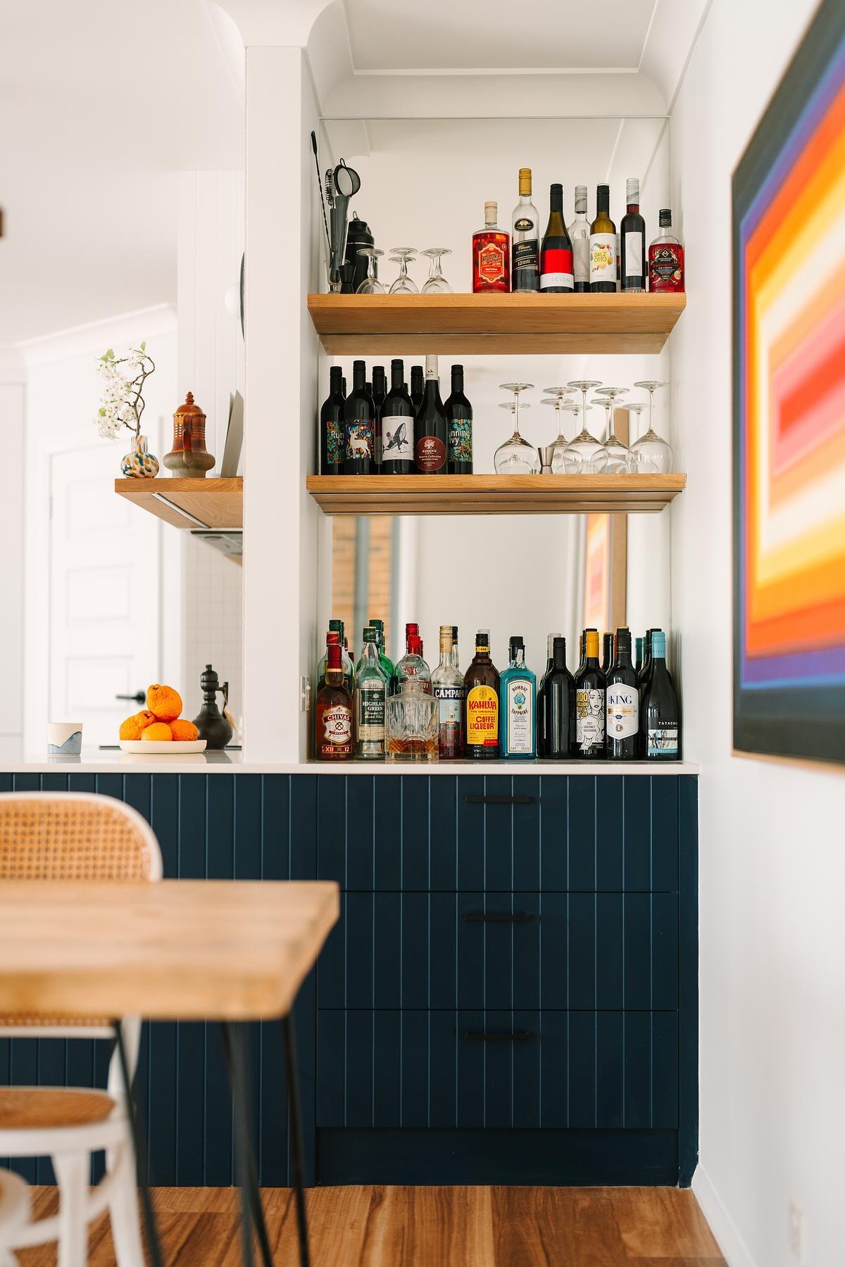 A former air-conditioning cavity was reimagined as a pocket gin bar, complete with warm wood shelves and a mirrored backing.