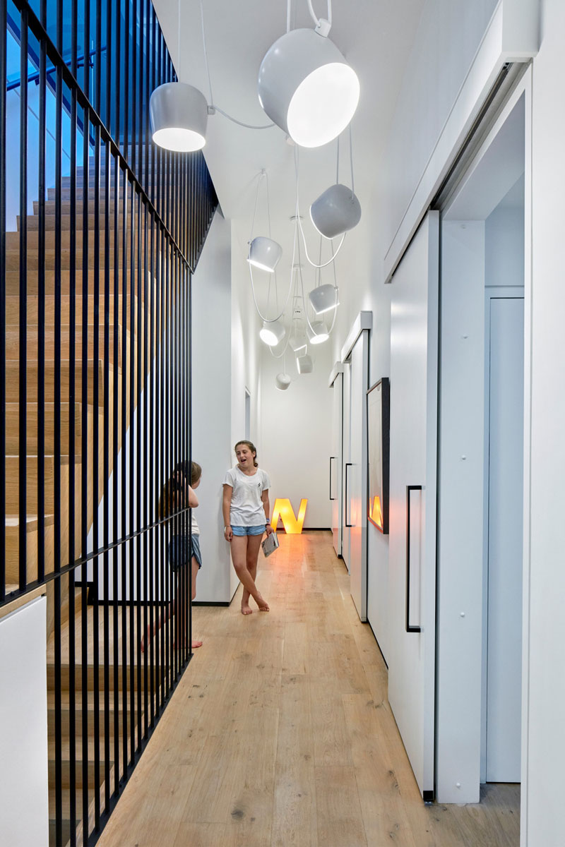Three children’s bedrooms are accessed through identical sliding doors, each space illuminated by hanging white pendant lights in the hallway. 