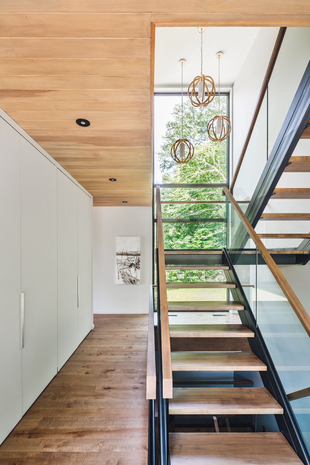 A glass-railed staircase topped with wood, is bathed in natural light connects all levels, keeping the interiors open and airy.