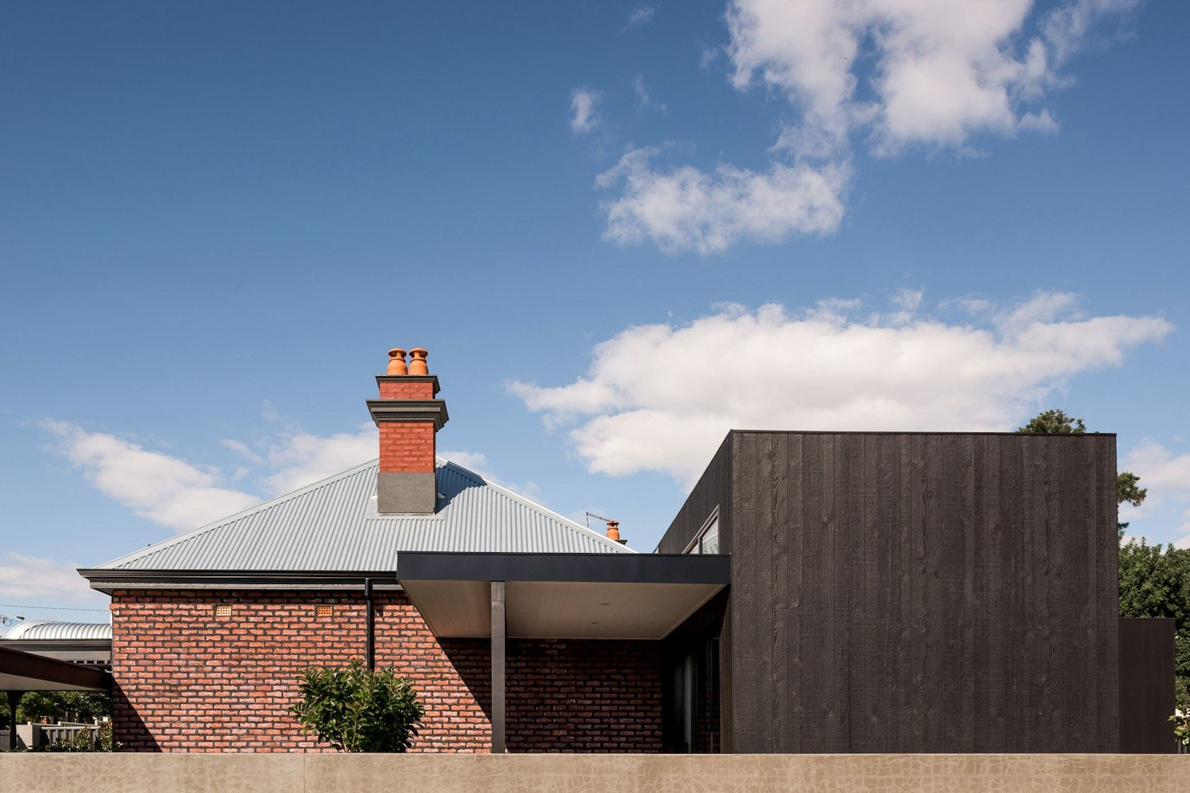A striking contrast between old and new defines this Australian heritage home renovation, featuring a dark modern extension and sleek carport