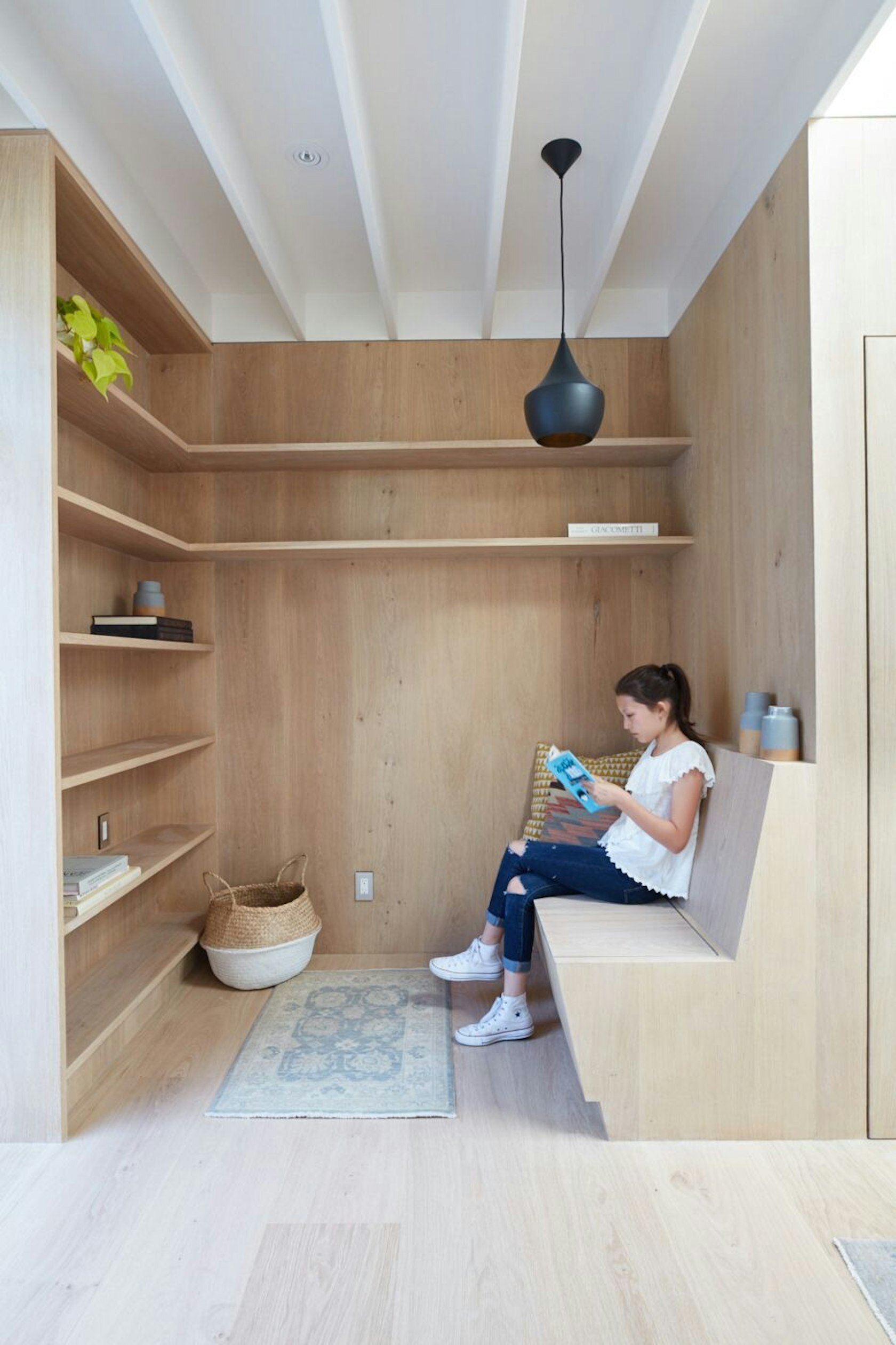 A cozy reading nook with a built-in bench and floor-to-ceiling bookshelves adds warmth and character to this small backyard studio.