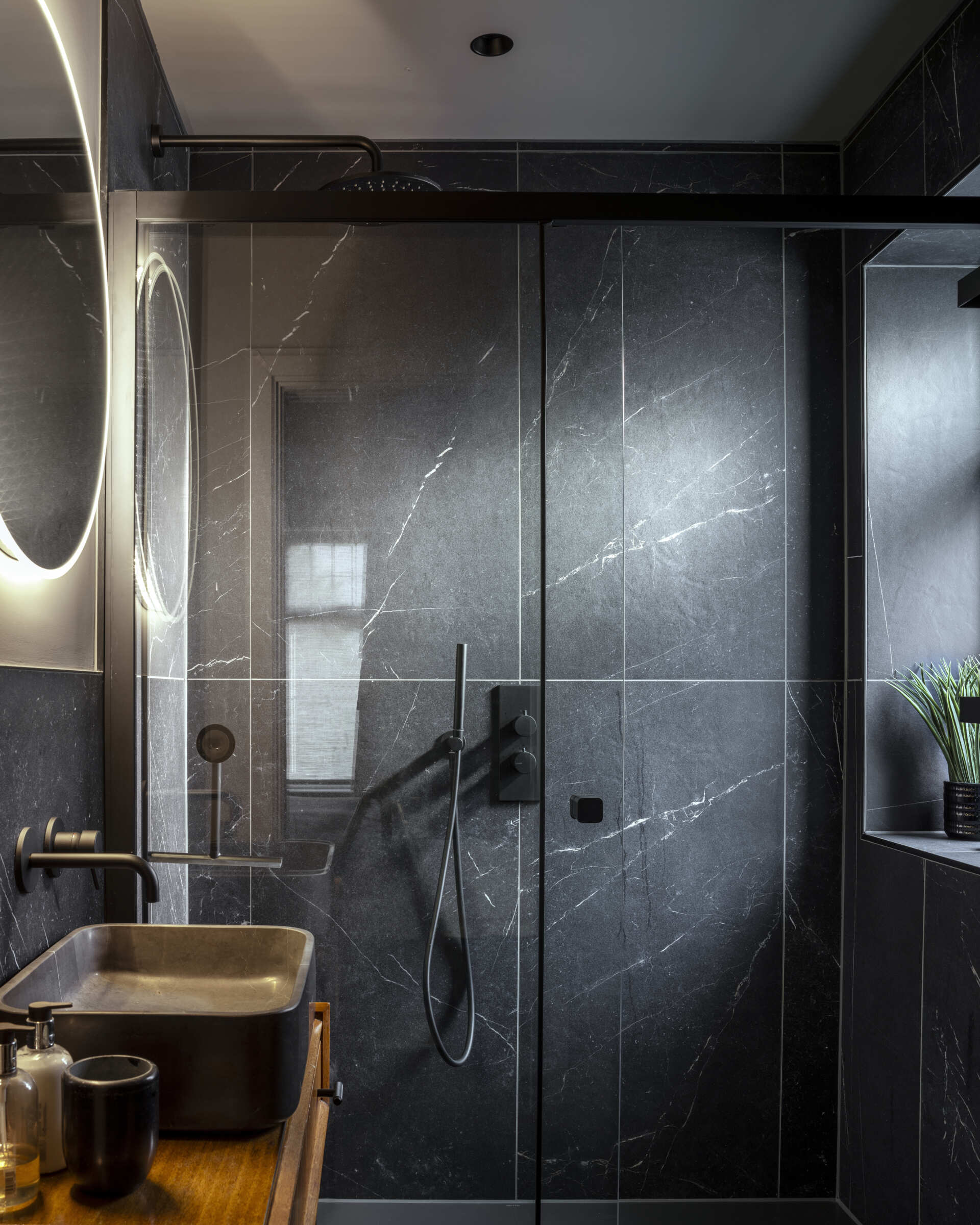 This bathroom continues the home’s theme of understated luxury, with oversized grey tiles, black accents, and a backlit mirror.