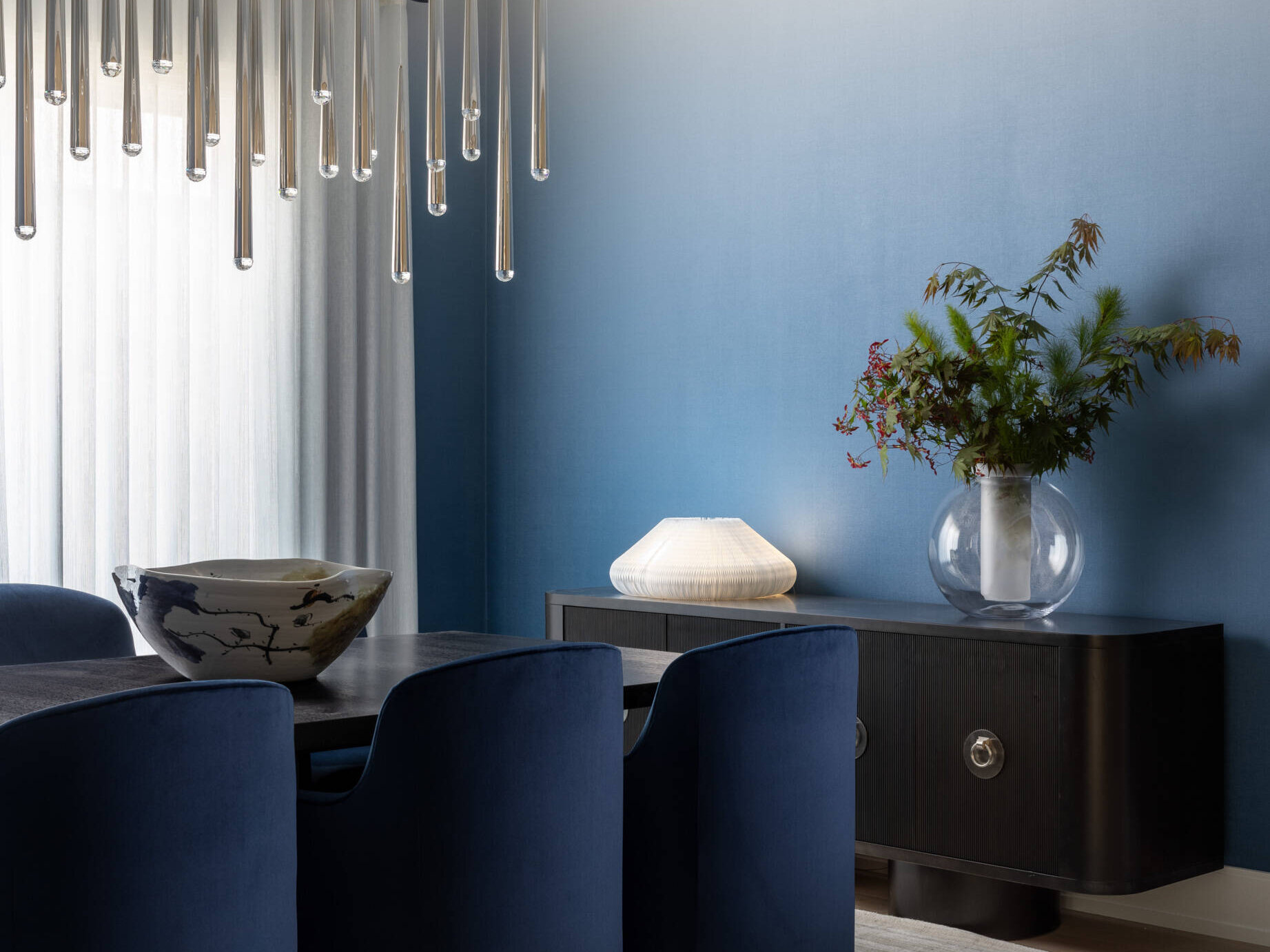 The dining room leans into atmosphere. A wood table, comfortable chairs, and a chandelier with a raindrop shimmer create a soft halo after dark. The walls carry gentle color, just enough to warm the scene without shouting. It is the kind of room that makes every dinner look like a celebration.