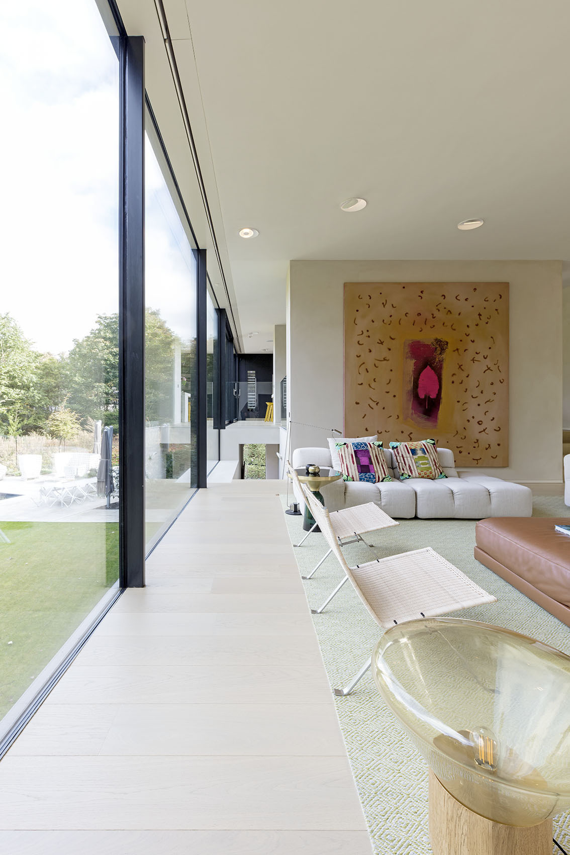 In the living room, a dark fireplace anchors the far wall, its tone a subtle echo of the home’s black facade. Vast windows frame the surrounding landscape, while floor-to-ceiling glass along the kitchen and living areas allows daylight to flood the space.