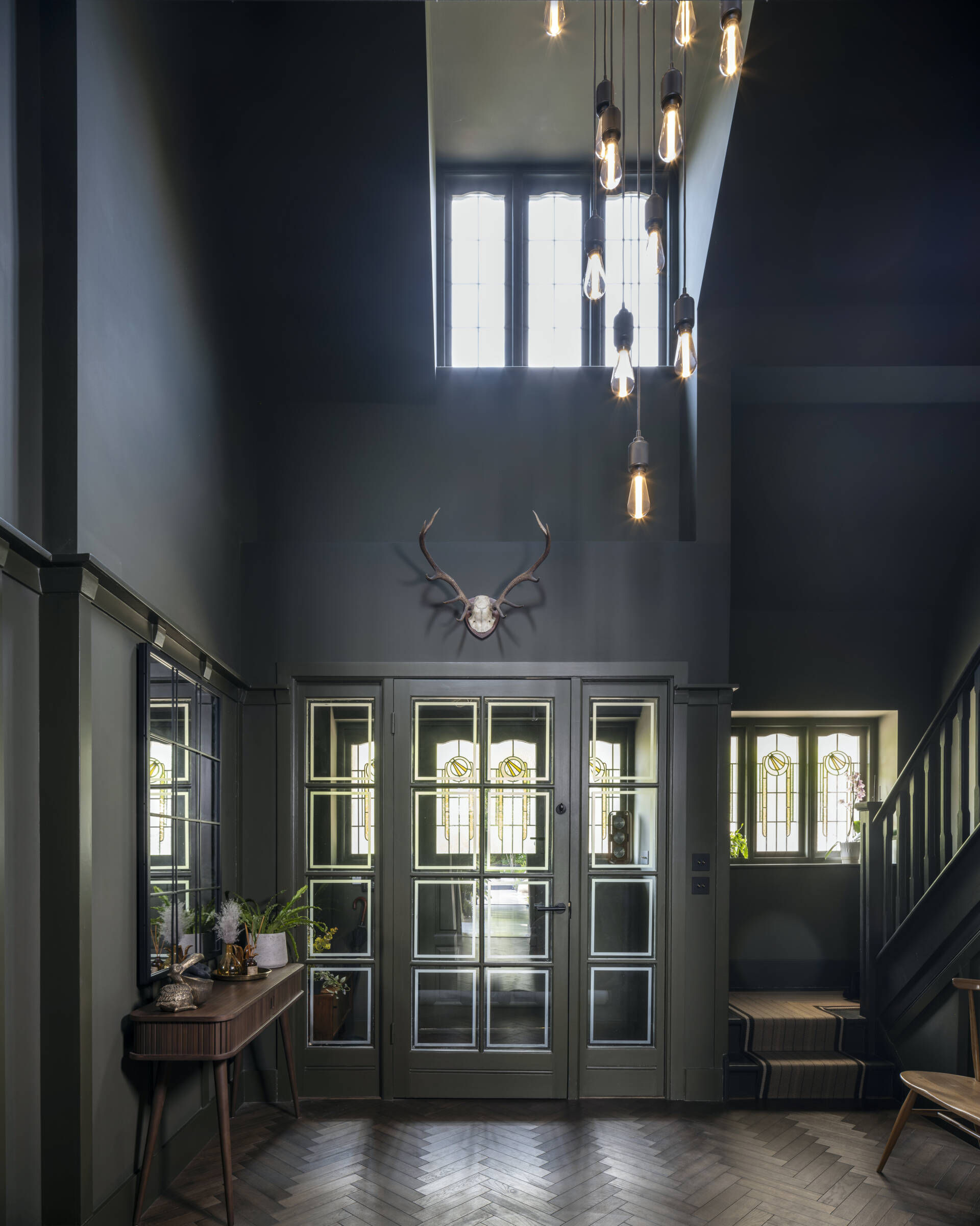 Stepping through the front door now reveals a sense of openness that didn’t exist before. The restored original staircase anchors the foyer, drawing the eye upward toward the light that filters through the new galleried stairwell.