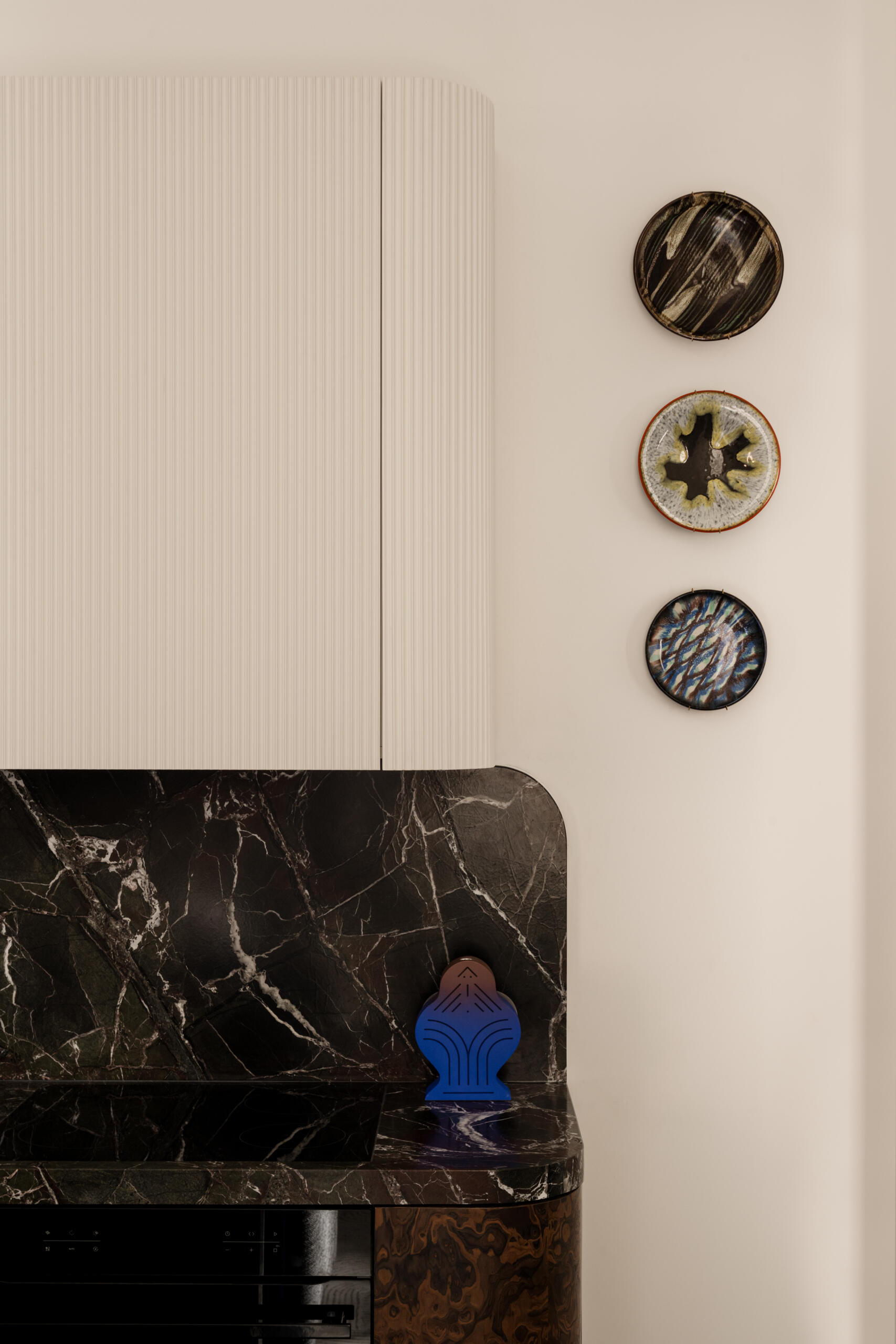 In the kitchen, a deep green Rosso Levanto marble meets California Burl veneer for a dramatic contrast. A burst of Chinese red inside the cabinets adds surprise, while a glossy ultramarine console defines the open-plan living area with bold color and precision.