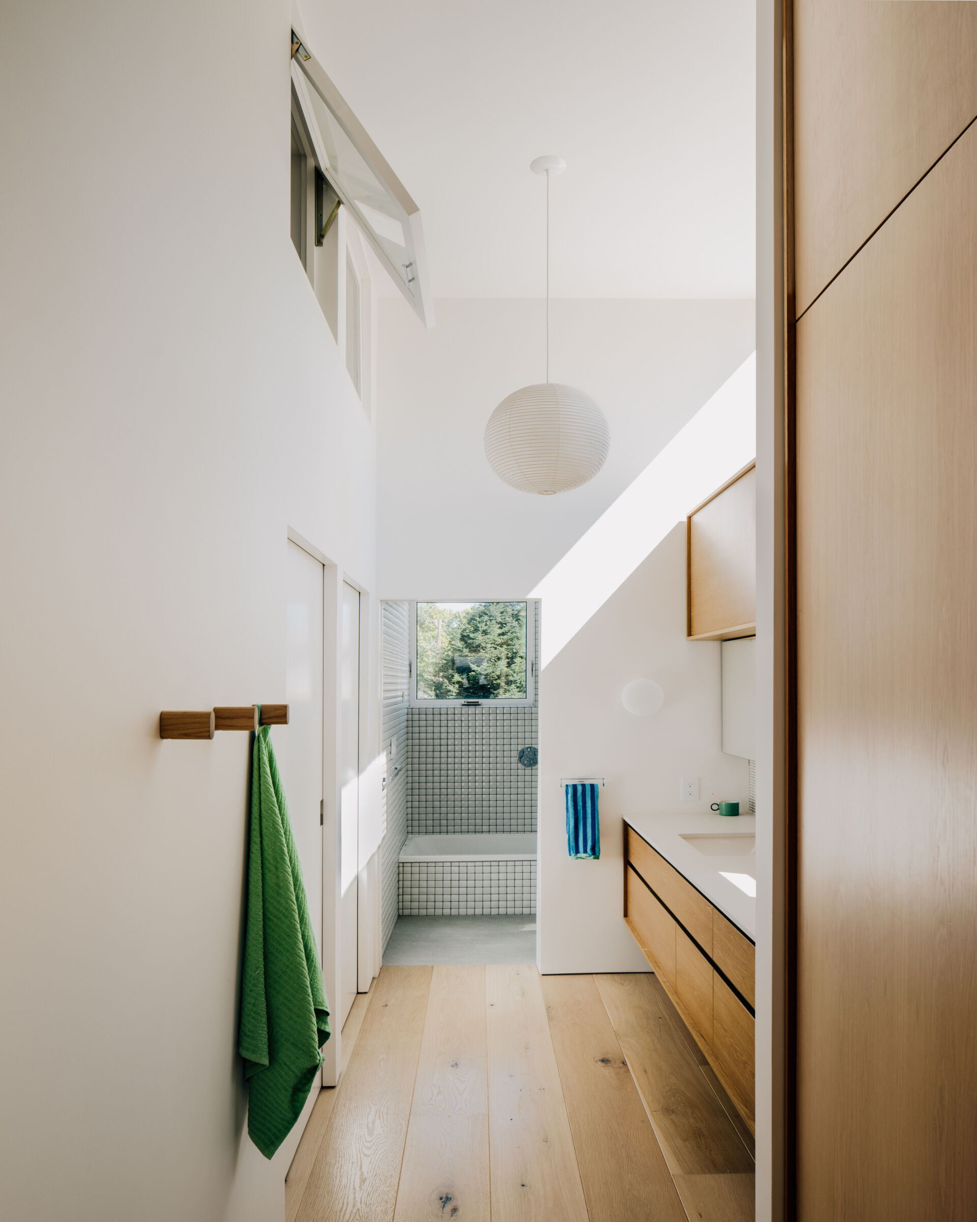 A small hallway hosts a wood vanity, while the bedrooms sit behind sliding doors on the opposite wall. A third sliding door at the end of the vanity reveals the built-in bathtub and toilet that's framed by small square tiles.