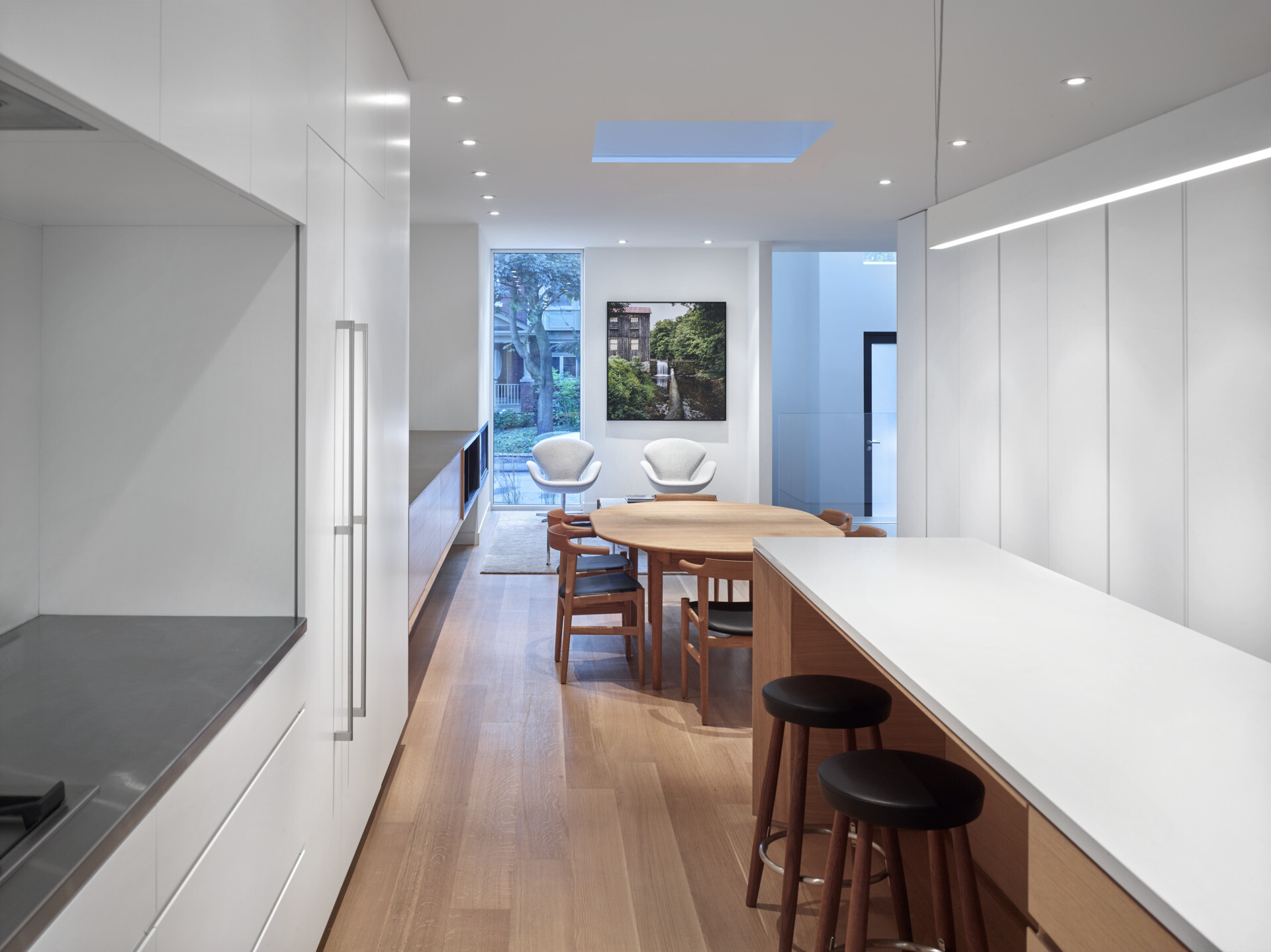 A minimalist white kitchen with a long island overlooks a sunken living area, connecting family life through clever design.