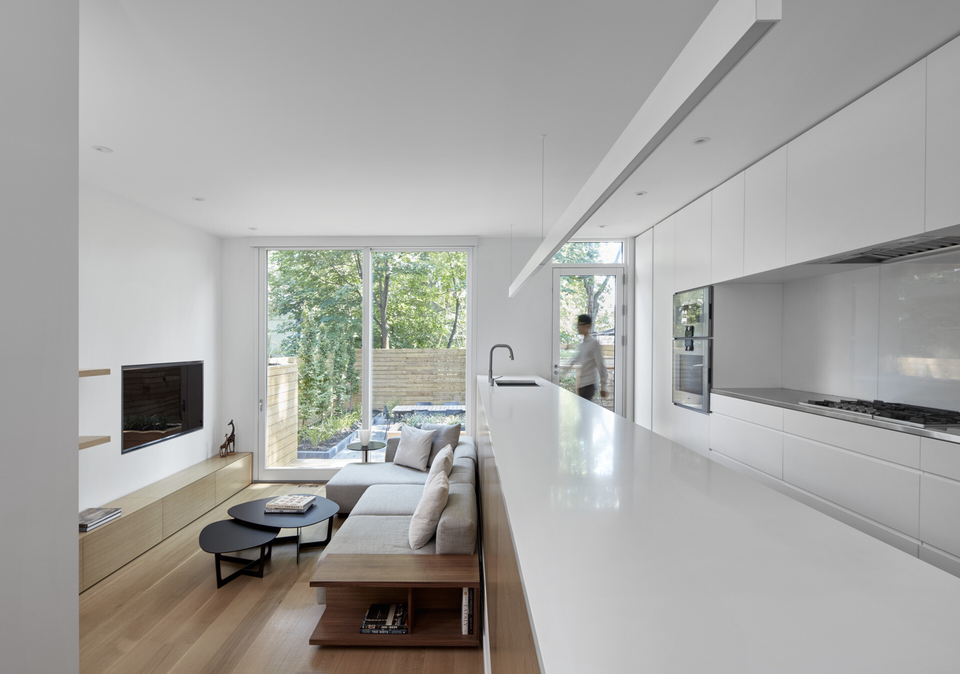 A minimalist white kitchen with a long island overlooks a sunken living area, connecting family life through clever design.
