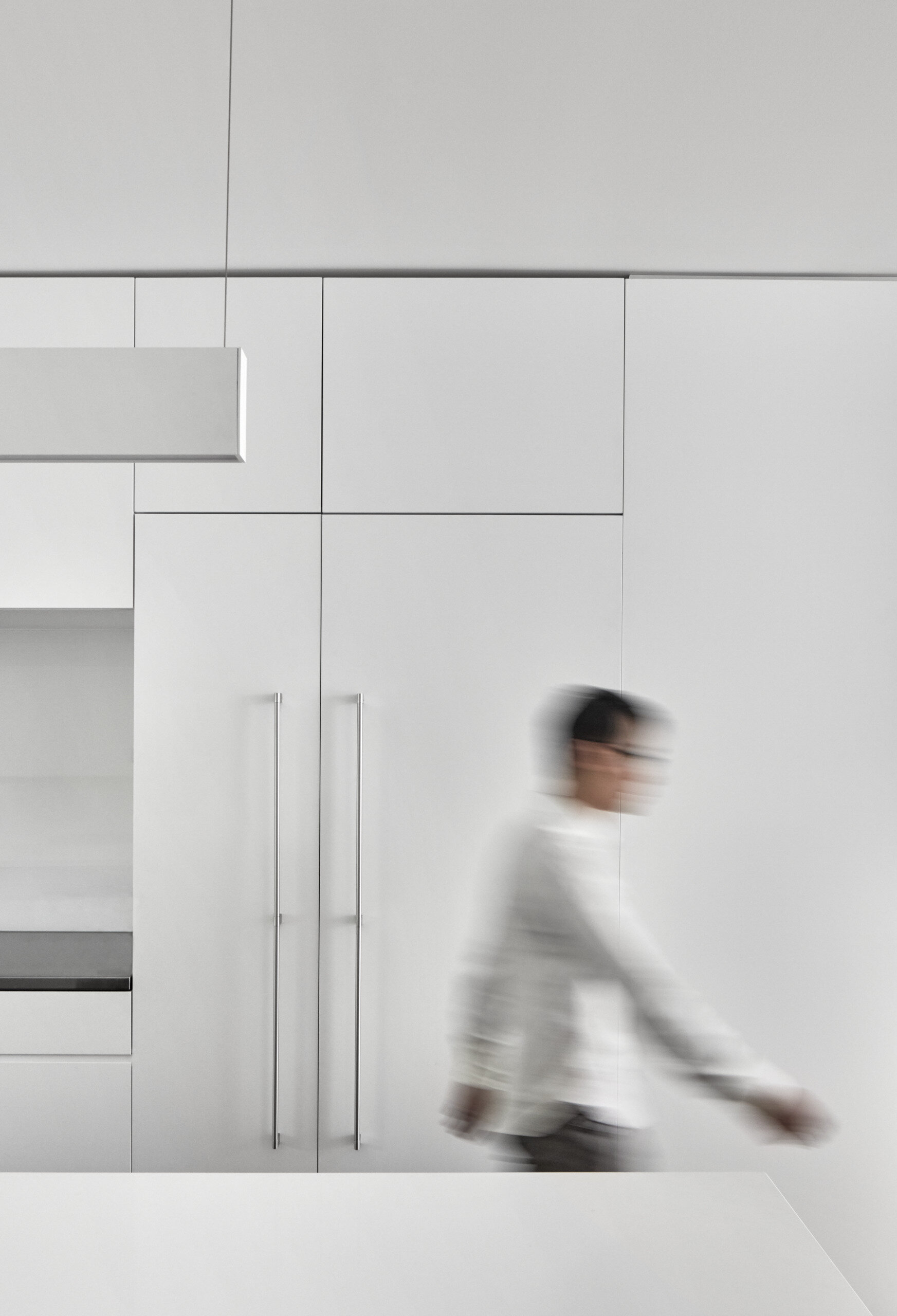A minimalist white kitchen with a long island overlooks a sunken living area, connecting family life through clever design.