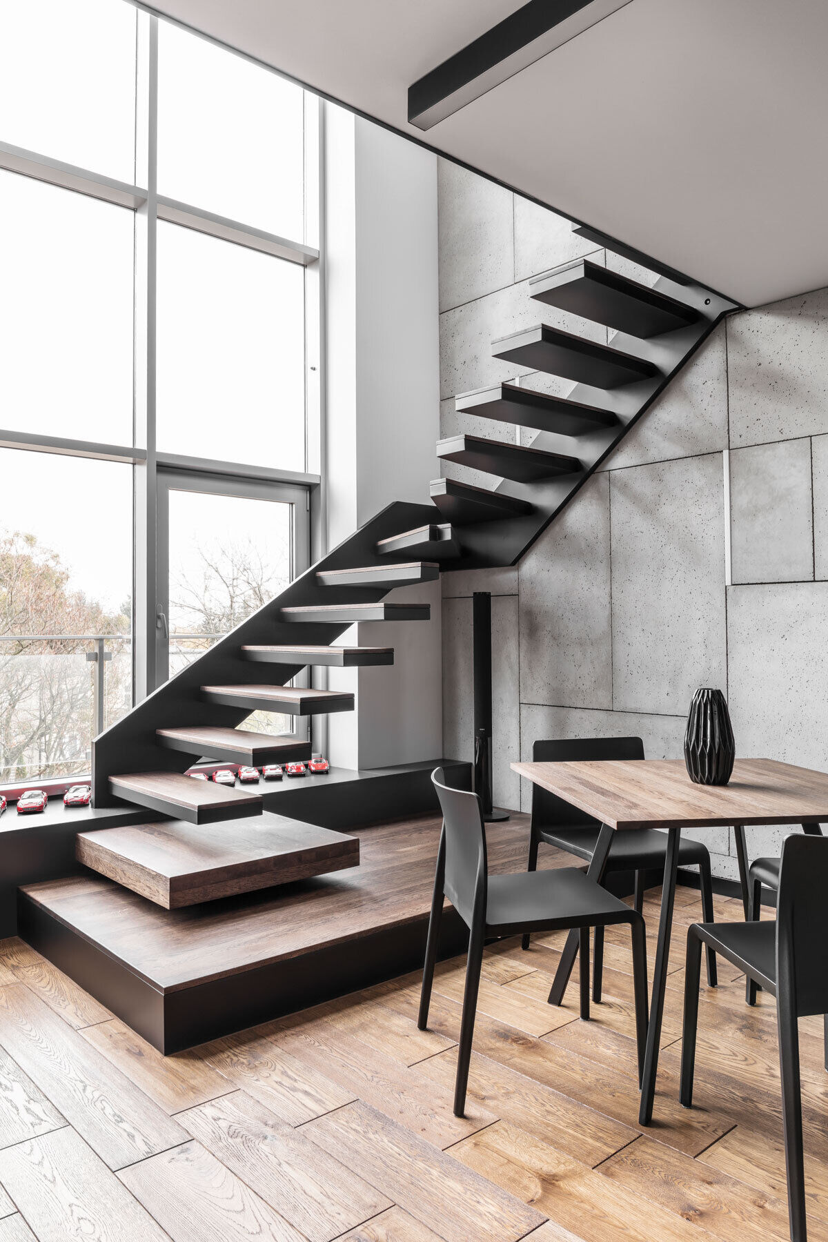Black steel stairs with wood treads lead from the living area to a mezzanine with a home office.