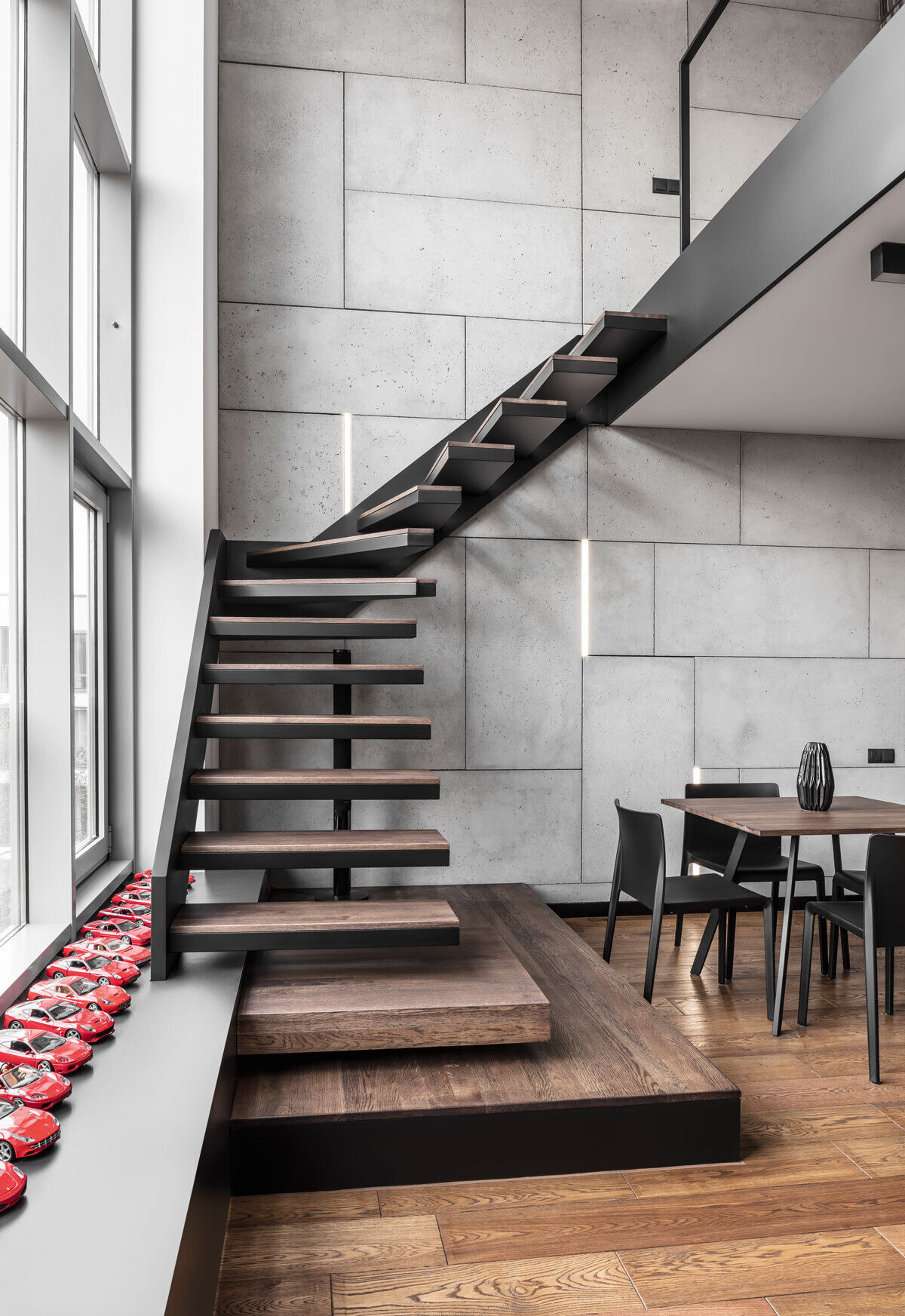 Black steel stairs with wood treads lead from the living area to a mezzanine with a home office.
