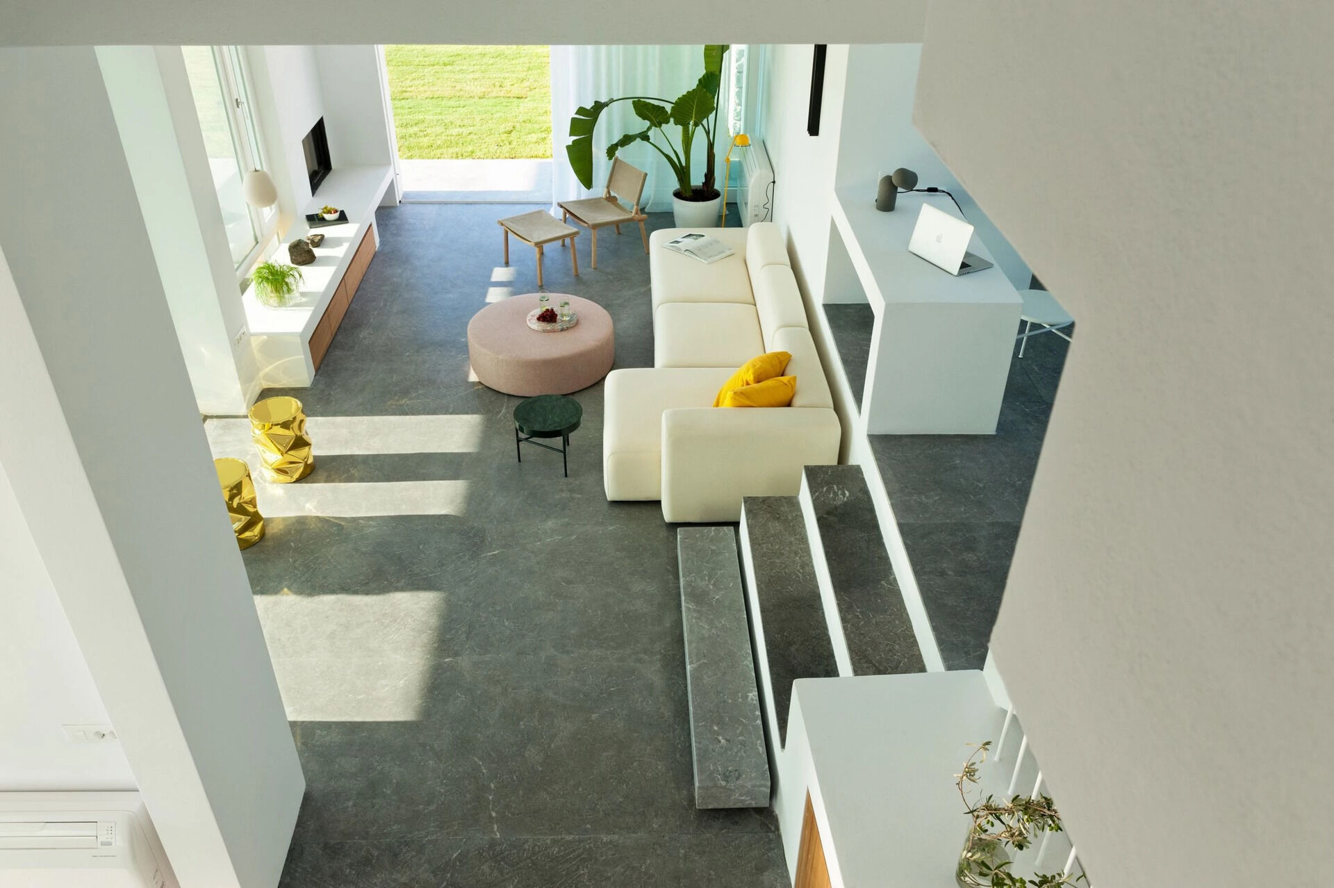 Inside, white plaster walls and grey cement floors create a calm canvas for wooden details and pops of color. The living room flows seamlessly to an outdoor lounge built around a palm tree.