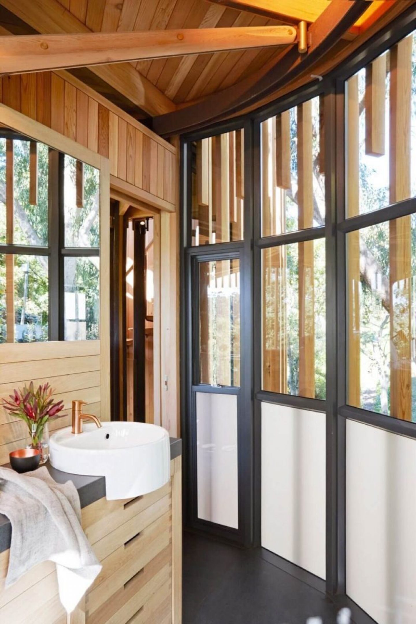 A refined mix of dark tiles, black-framed windows, and a brass faucet over a light wood vanity.