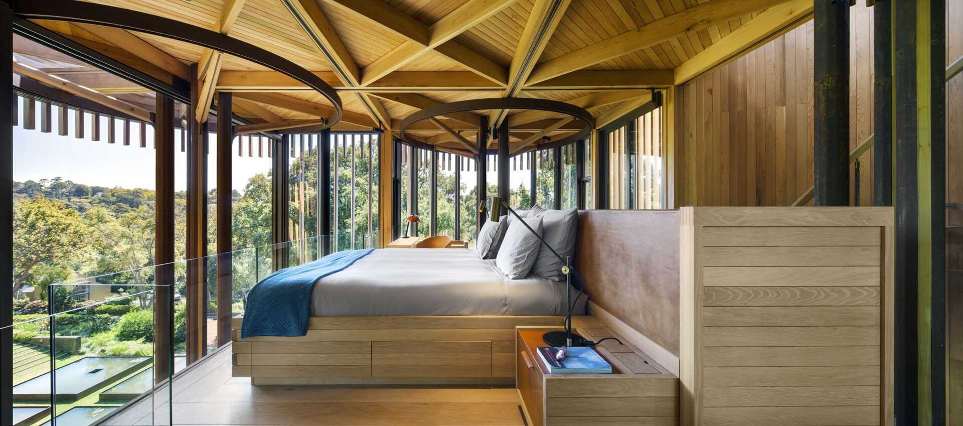 Floor-to-ceiling windows and a glass railing frame the bedroom’s elevated view into the treetops.