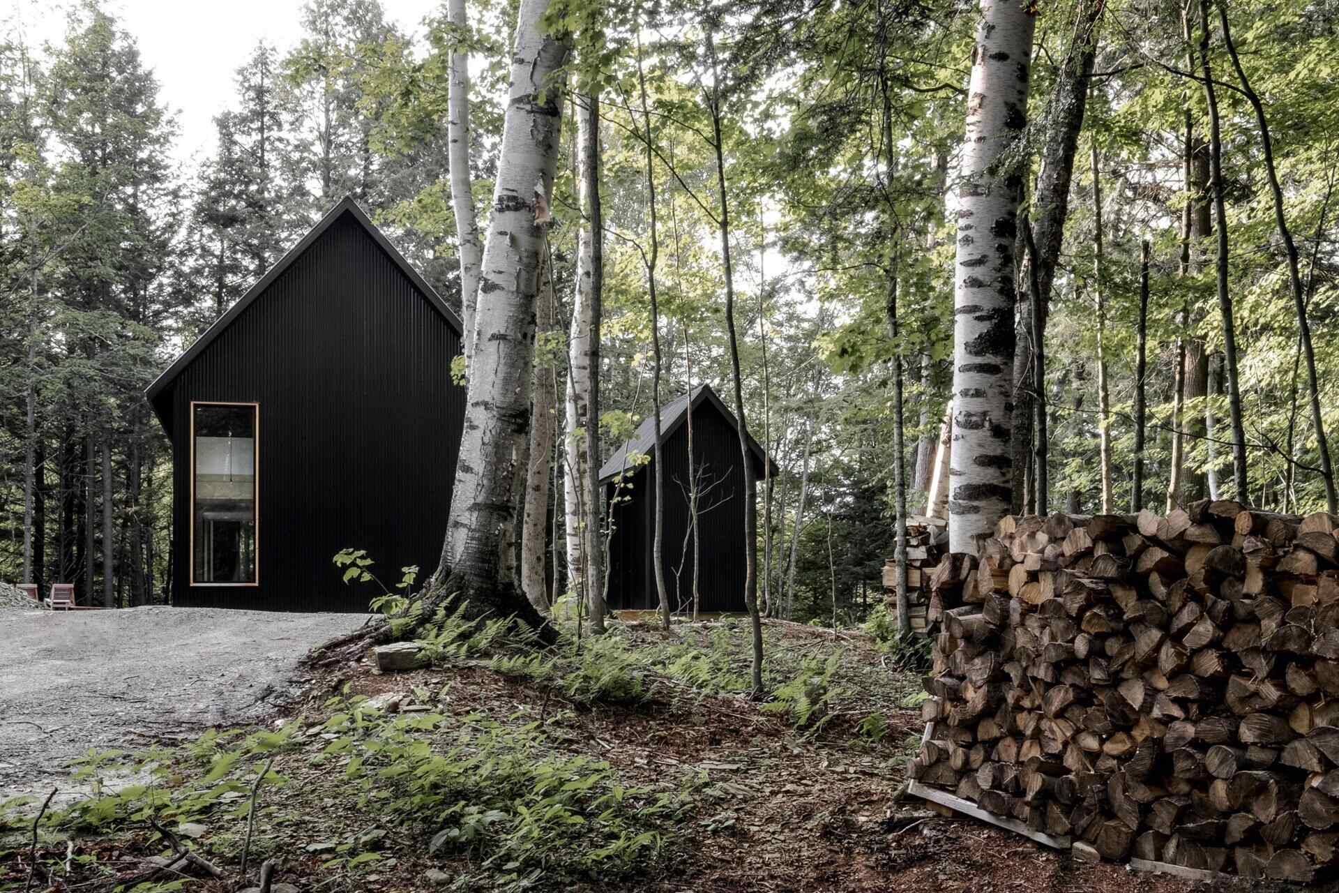 A striking black cottage tucked in a Quebec forest, blending modern design with traditional chalet forms for a moody, minimalist retreat.