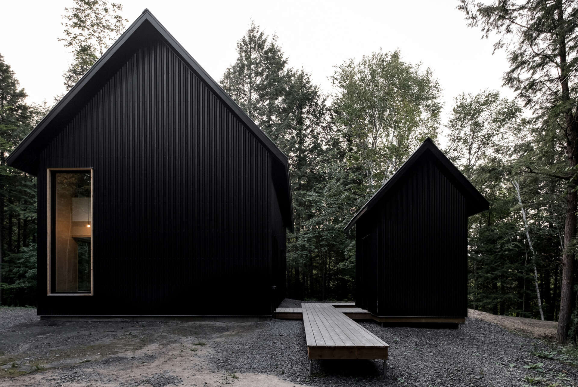 A striking black cottage tucked in a Quebec forest, blending modern design with traditional chalet forms for a moody, minimalist retreat.